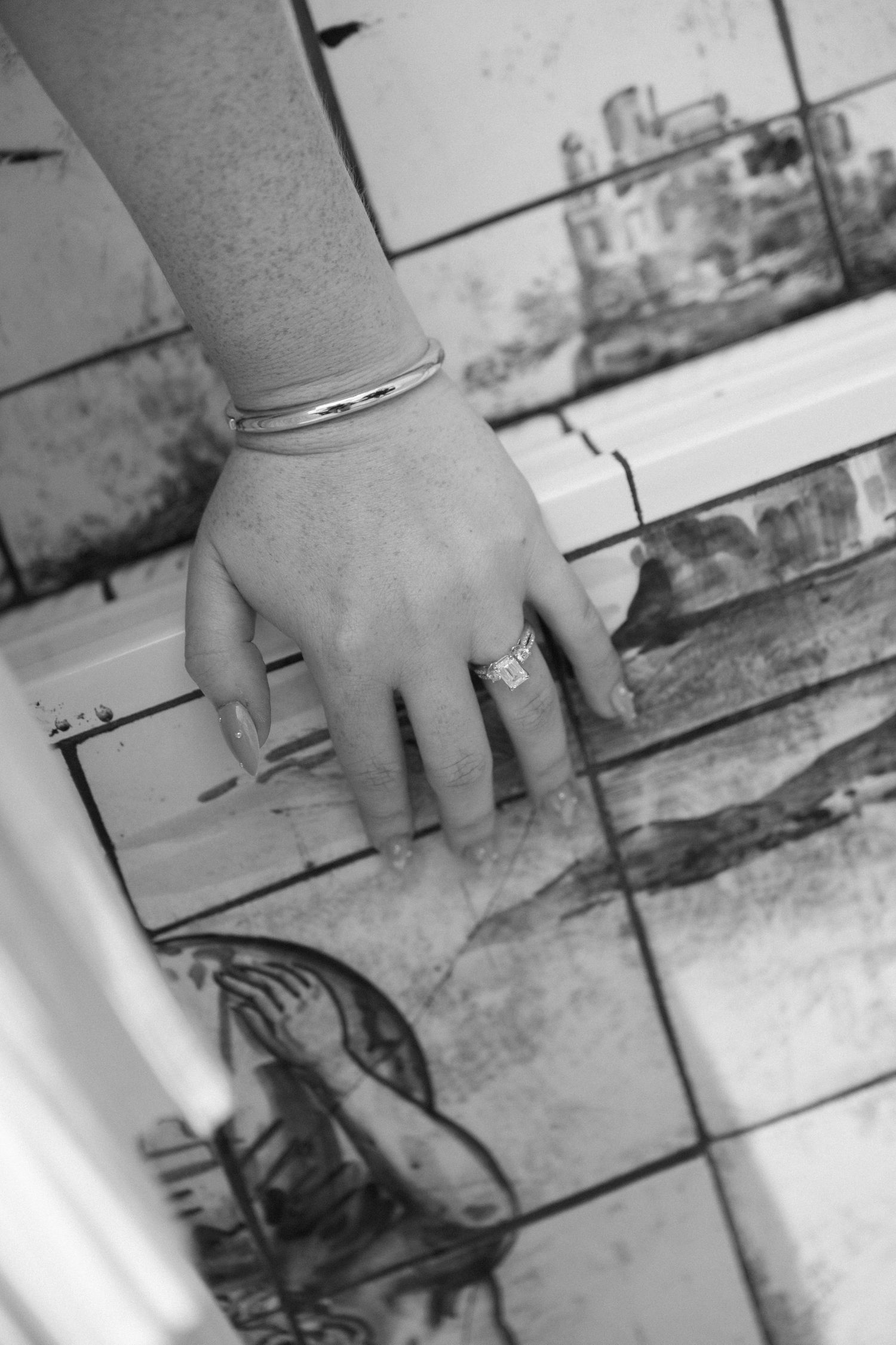Close-up of woman's hand with silver ring and bangle bracelet resting on decorative vintage tiles.