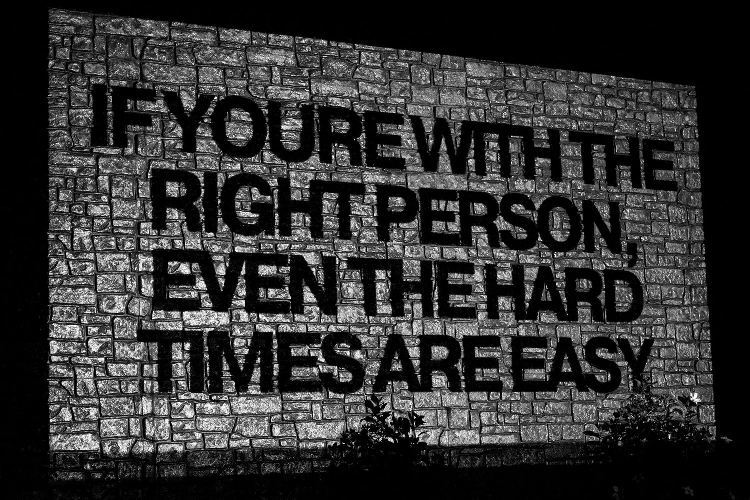 Black and white graffiti text on brick wall reads inspirational message about perseverance through hard times.