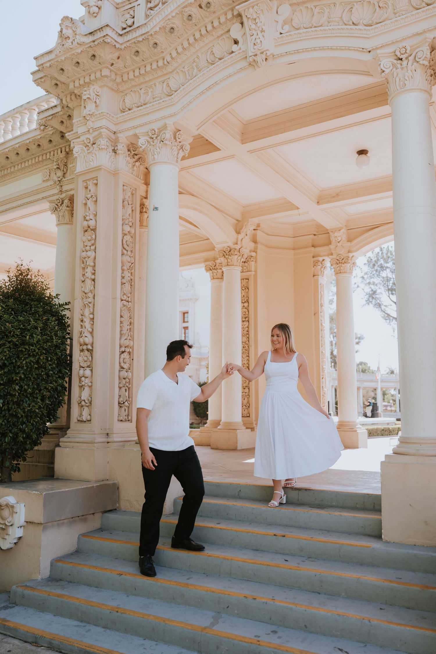 Couple dancing on ornate white marble steps of elegant classical building with decorative columns.