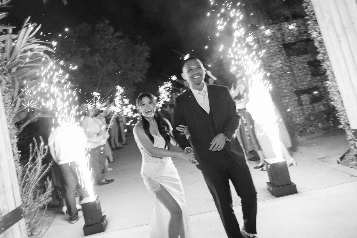 A couple runs through sparklers at night during a wedding celebration exit.