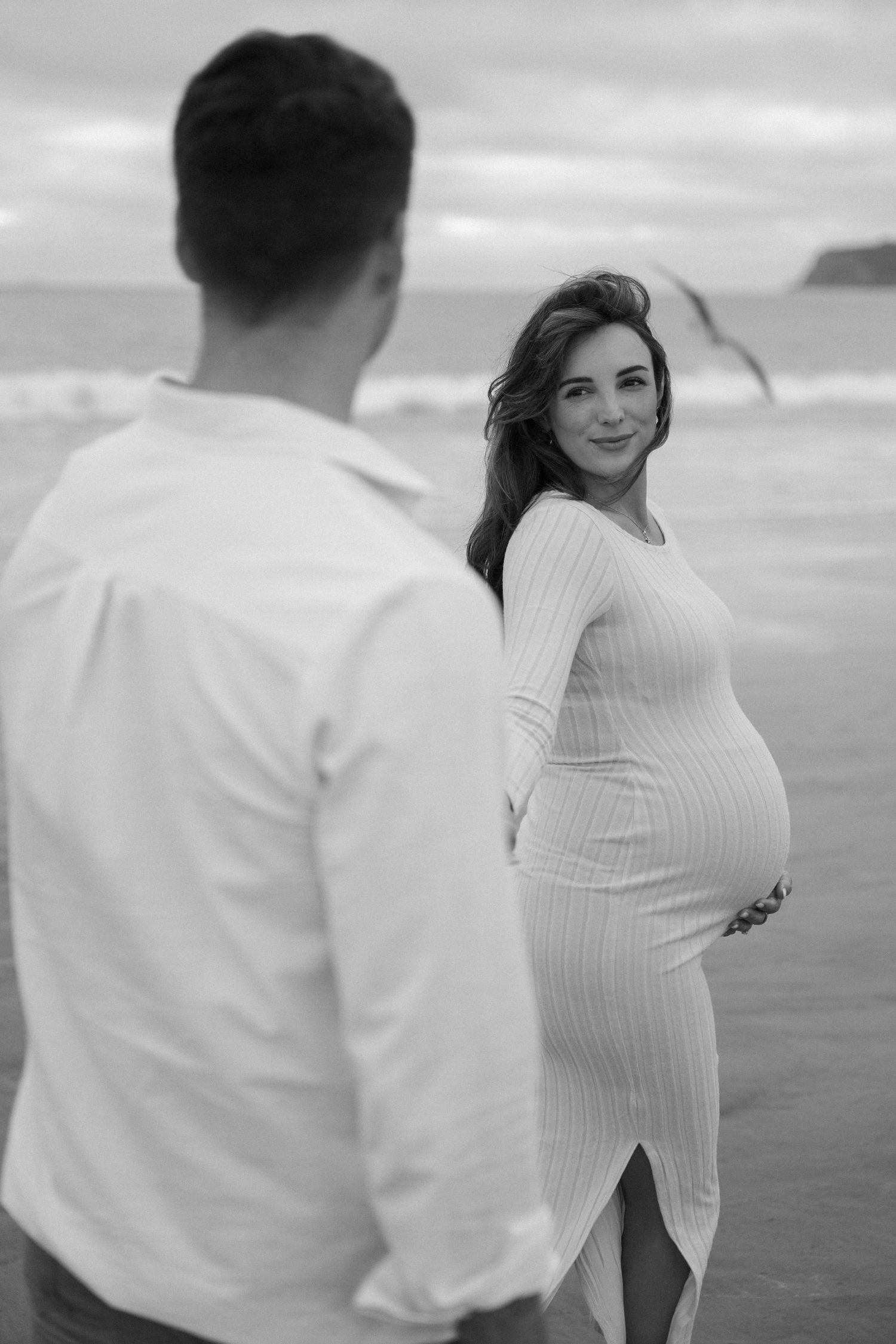 Romantic coastal photoshoot with couple in white attire against ocean backdrop.