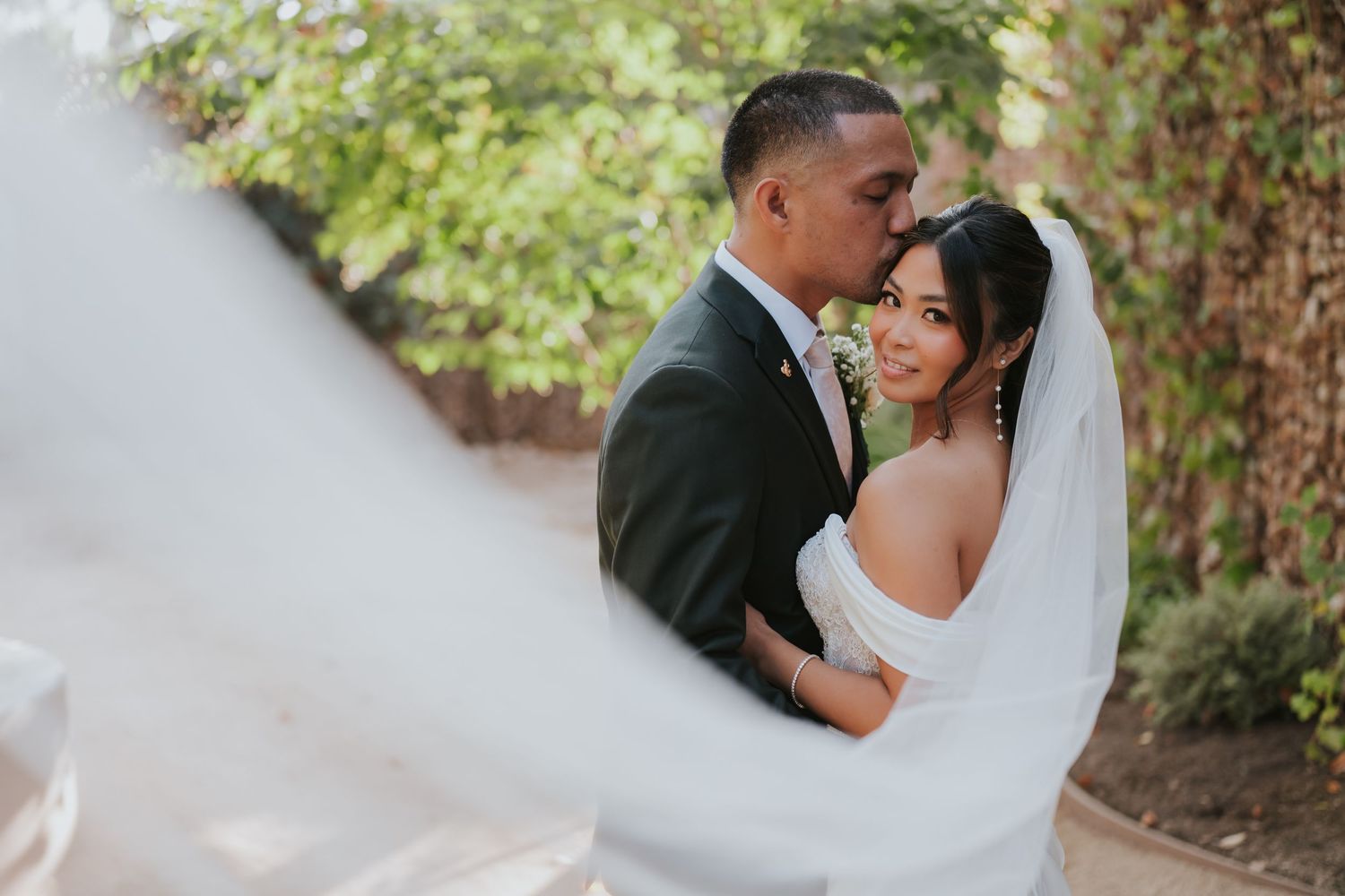 A romantic wedding couple embraces outdoors surrounded by lush greenery on their special day.