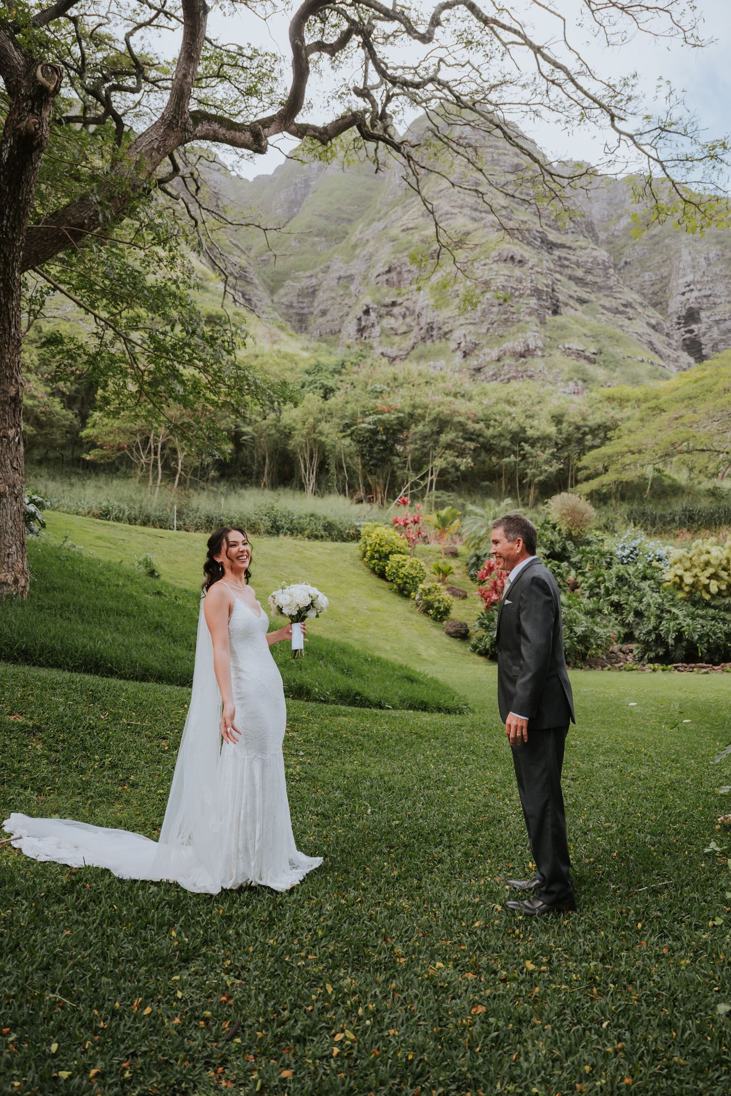 A couple shares an intimate moment on a scenic grassy slope with mountains in the background.
