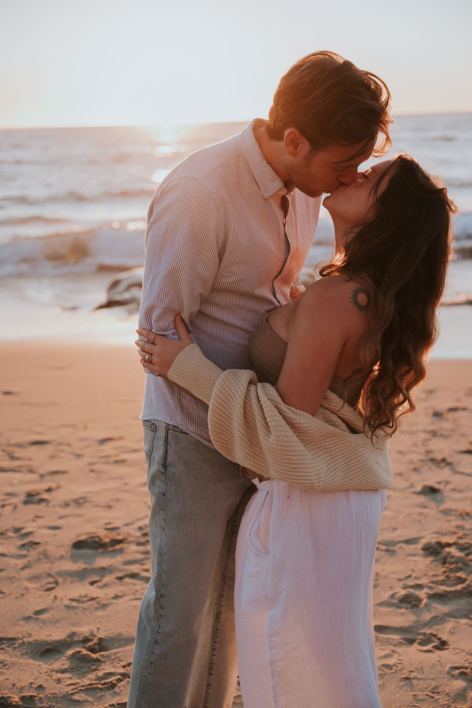 A romantic couple embraces on a sandy beach at sunset creating an intimate silhouette against the ocean backdrop.