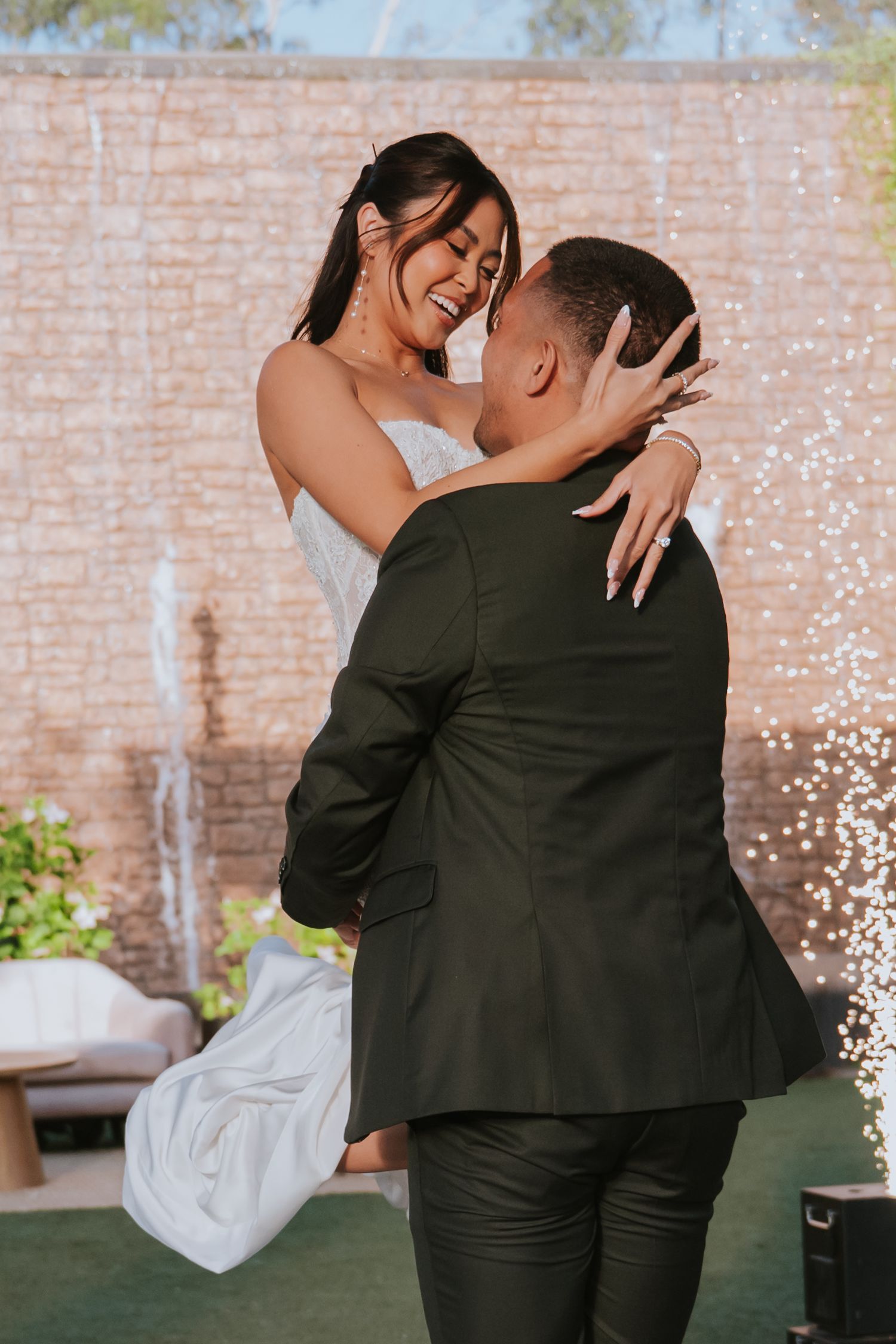 A couple shares an intimate dance together at a wedding reception with brick walls and greenery in the background.