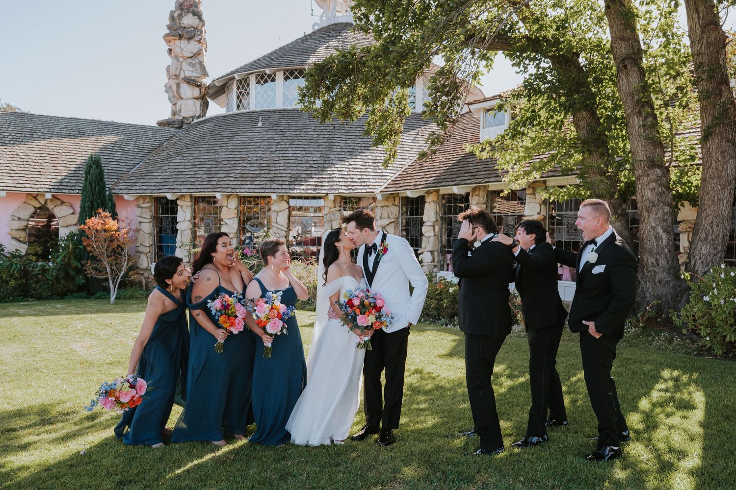 Wedding party poses together outdoors in a garden setting with trees and natural lighting.