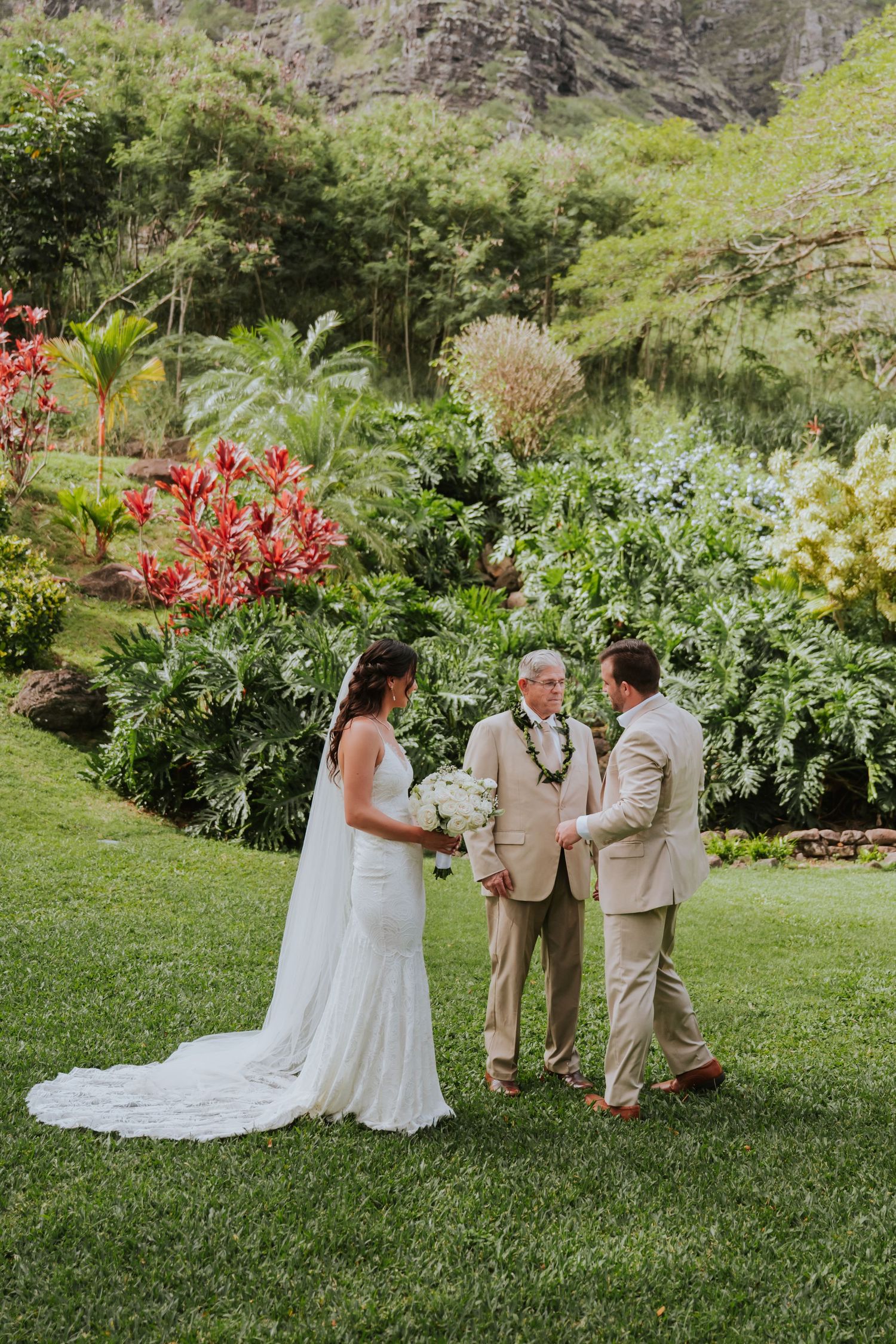 Wedding ceremony in a lush garden with red flowers and mountains in the background.