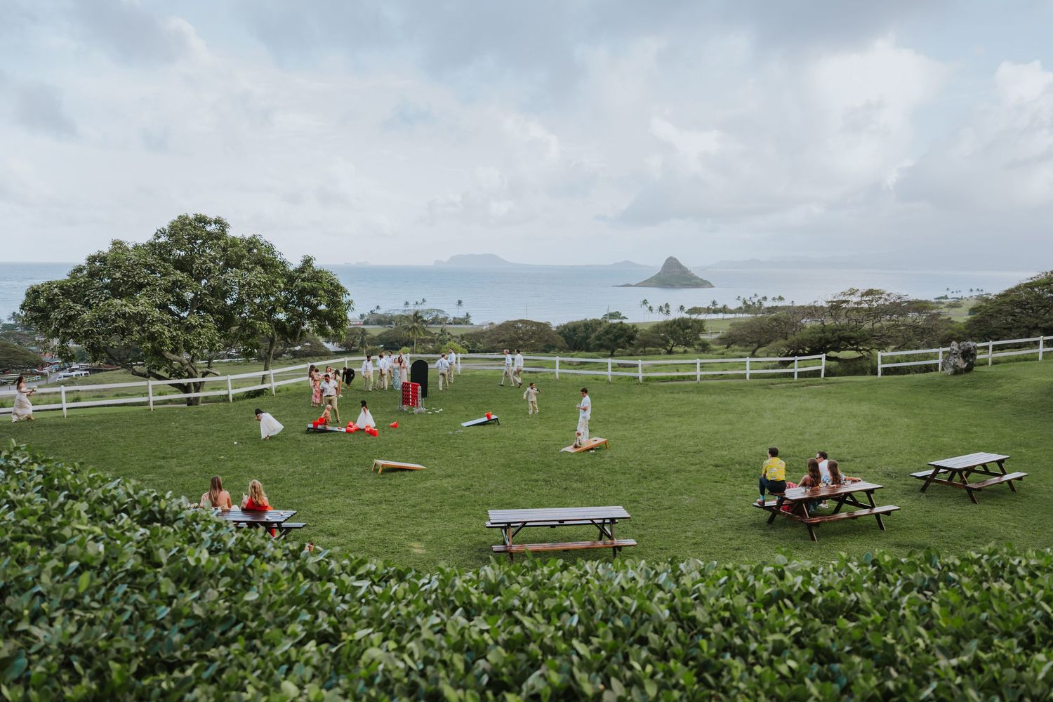 Scenic outdoor wedding venue with rolling green hills and picnic tables set against a cloudy mountain backdrop.