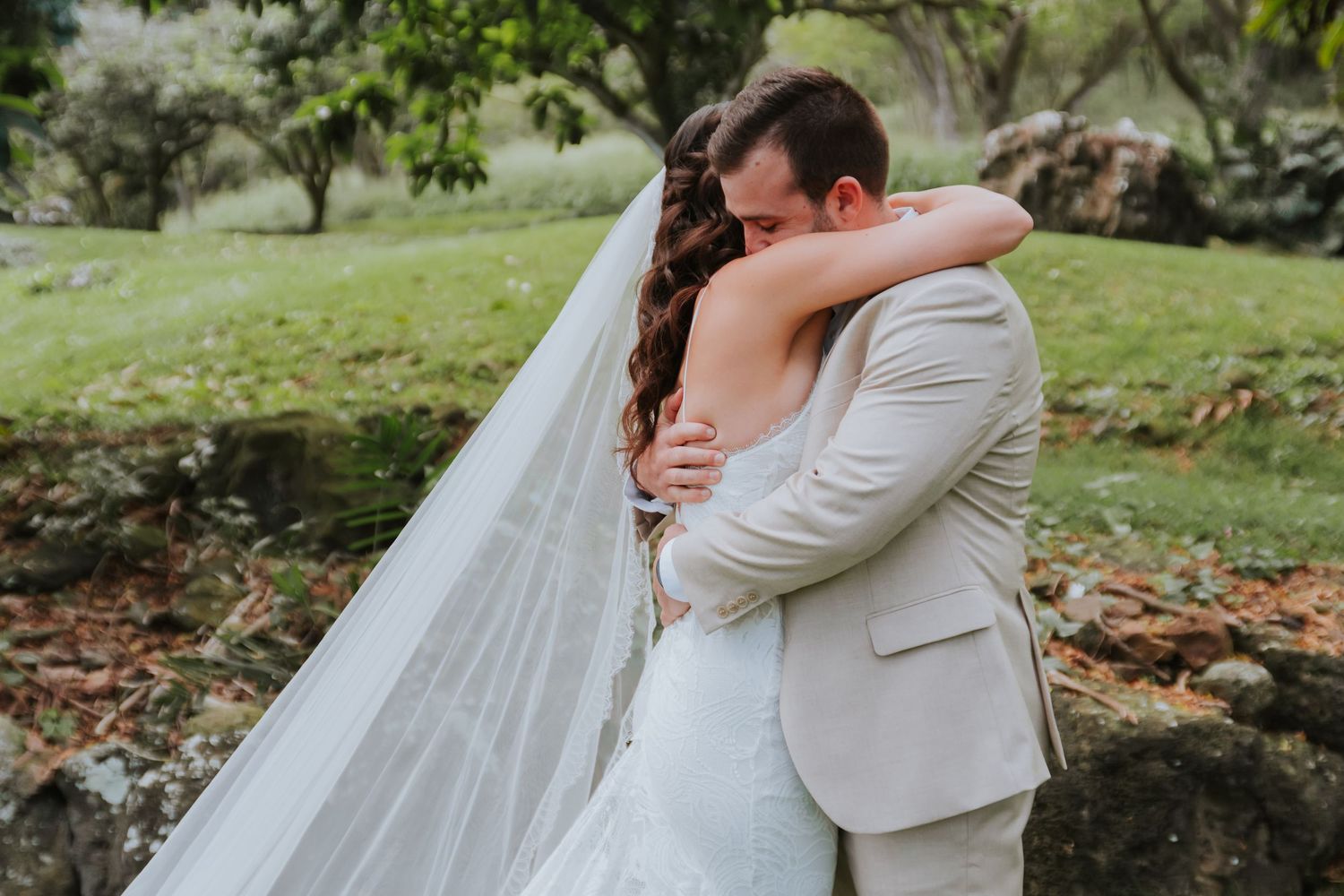 Romantic outdoor wedding scene with couple embracing in a lush garden setting with natural greenery.
