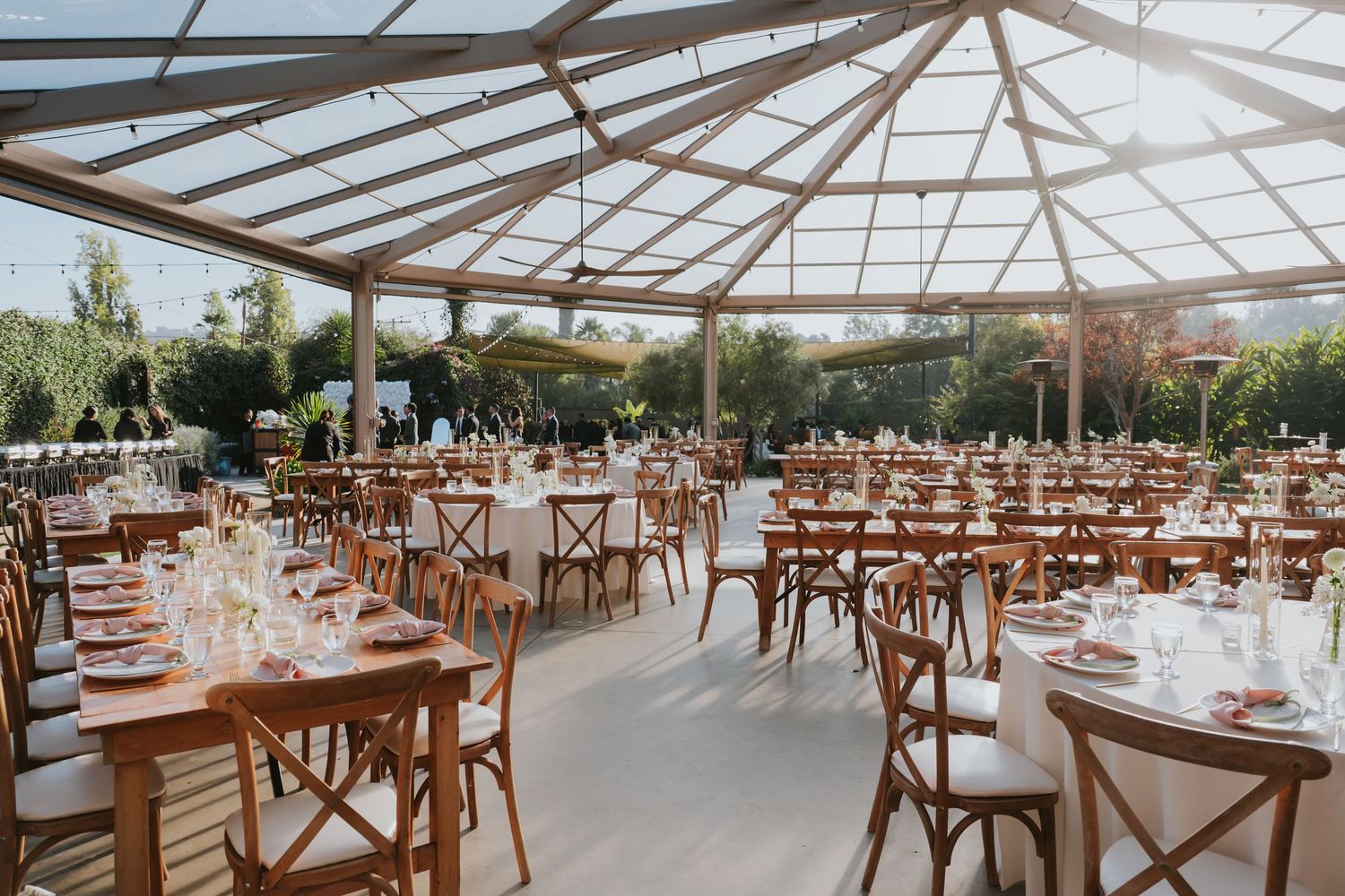 Elegant wedding reception venue with wooden cross-back chairs and glass ceiling letting in natural light.
