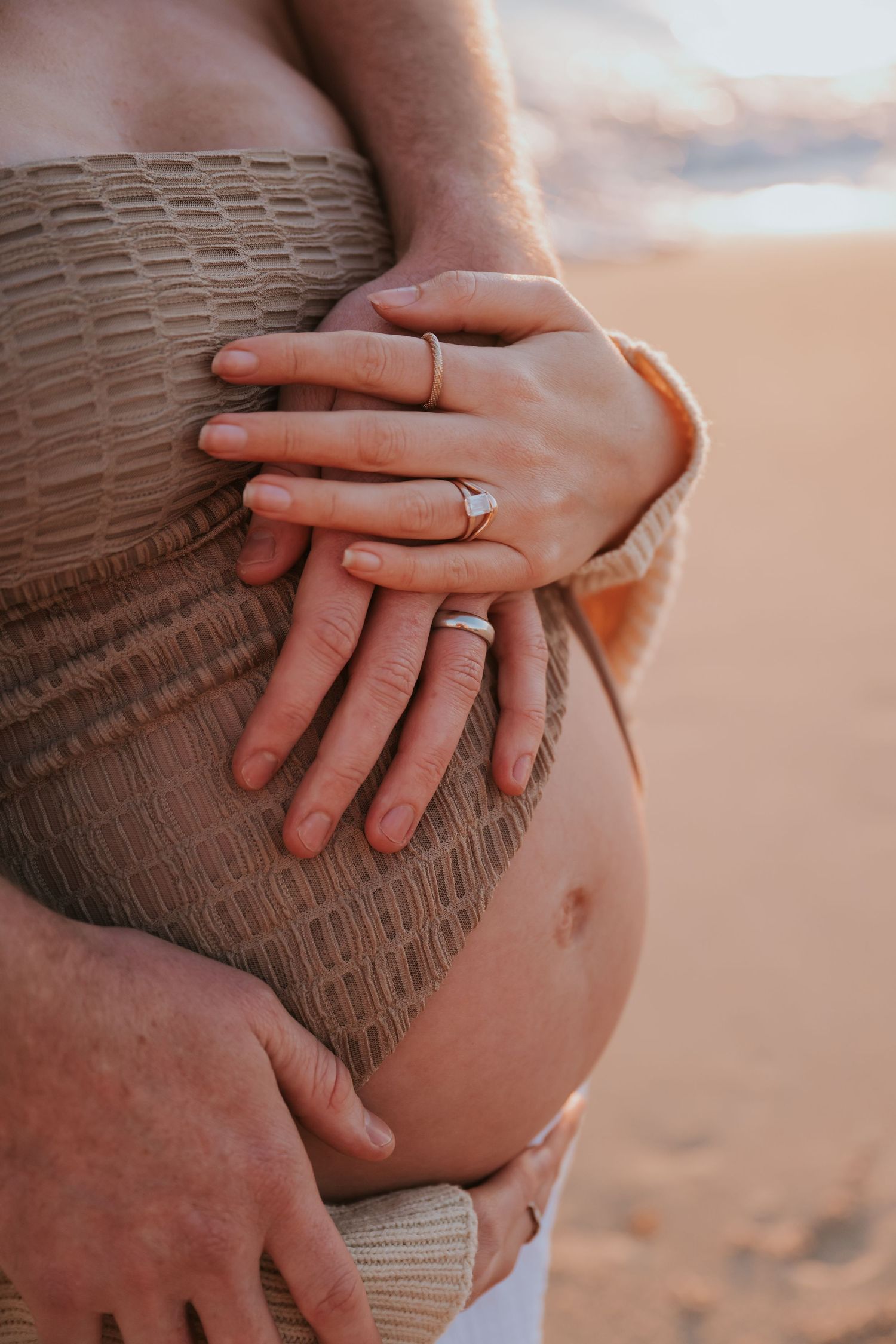 Close-up series of hands gently resting on a pregnant belly wearing a brown knit sweater in warm lighting.