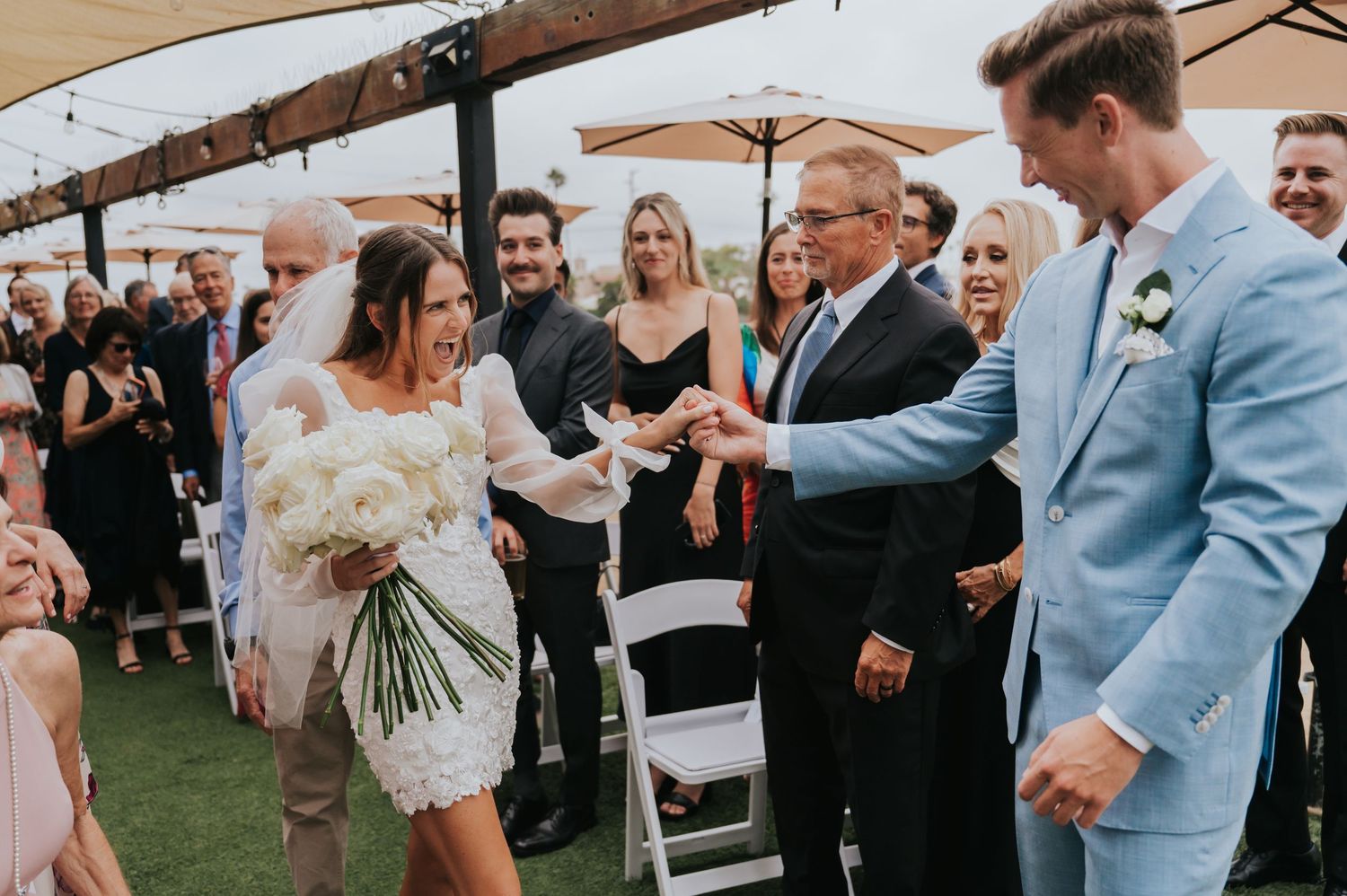 Wedding guests in formal attire celebrate and dance together at an outdoor reception venue.