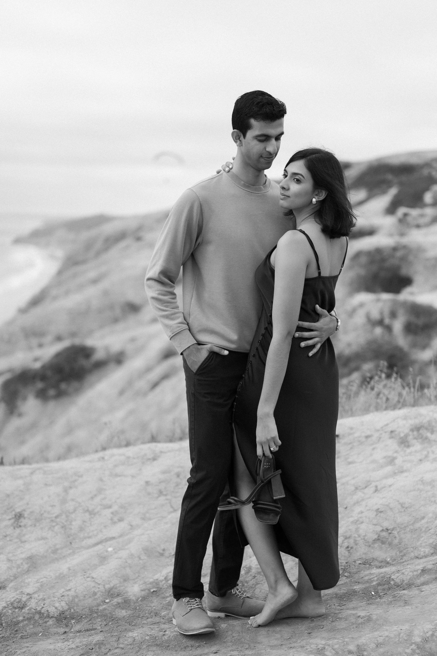 Black and white engagement photos captured on rugged coastal cliffs.