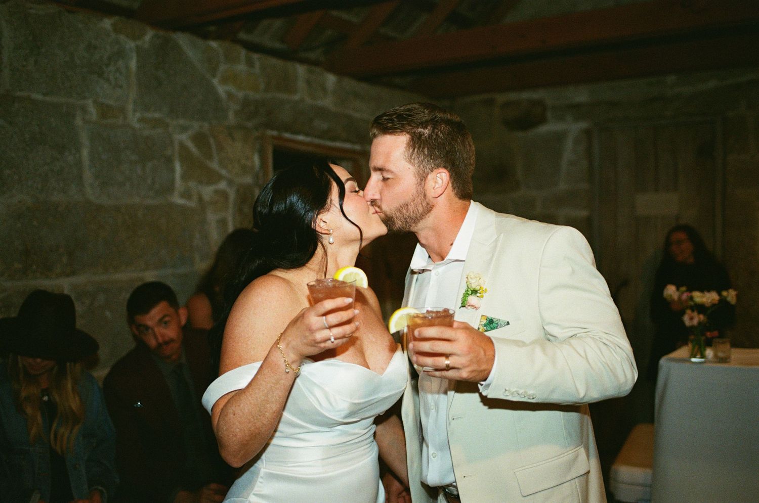 Bride and groom sharing a kiss while holding drinks at their wedding reception.