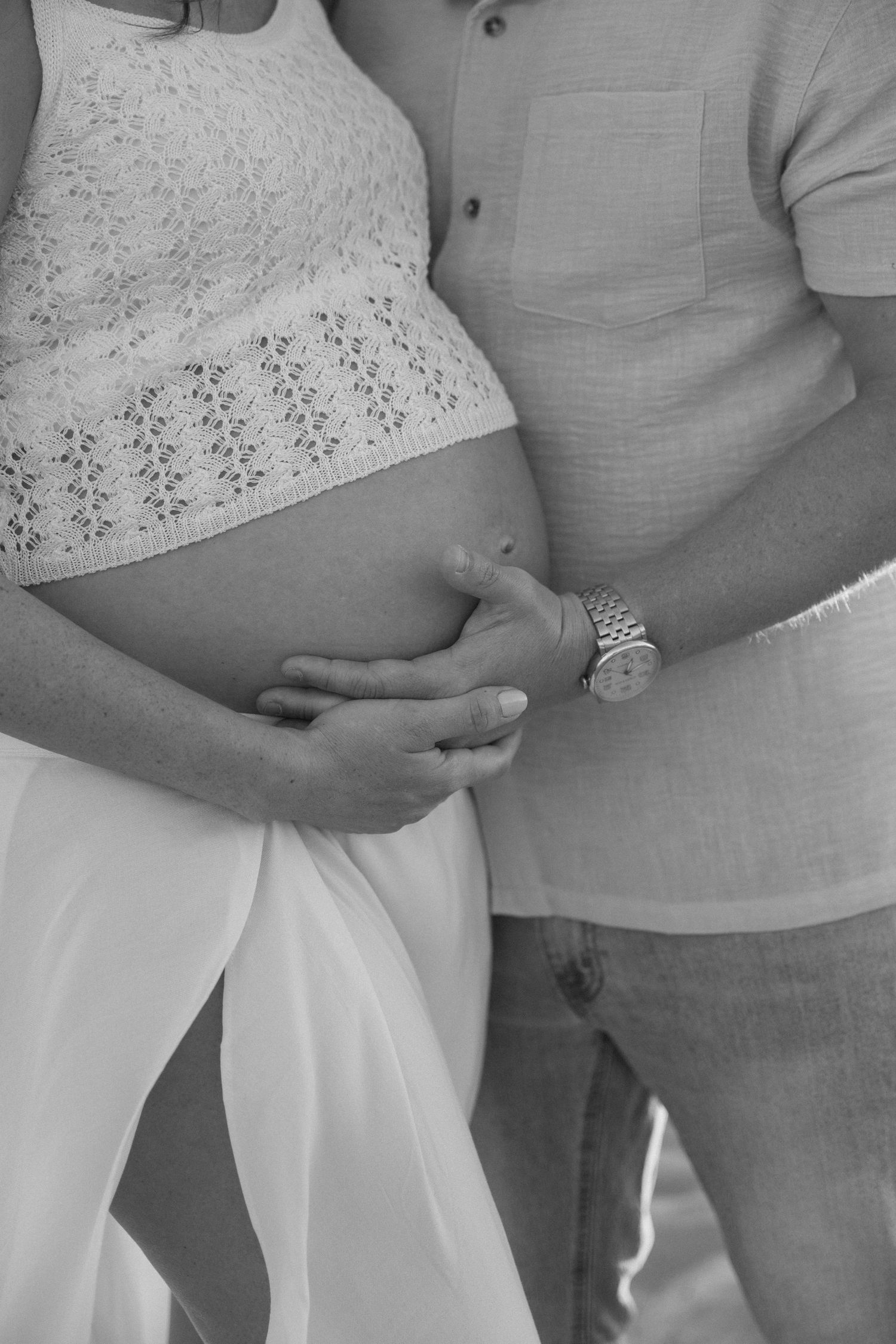 Black and white photo of a pregnant woman and her partner tenderly cradling her baby bump together.