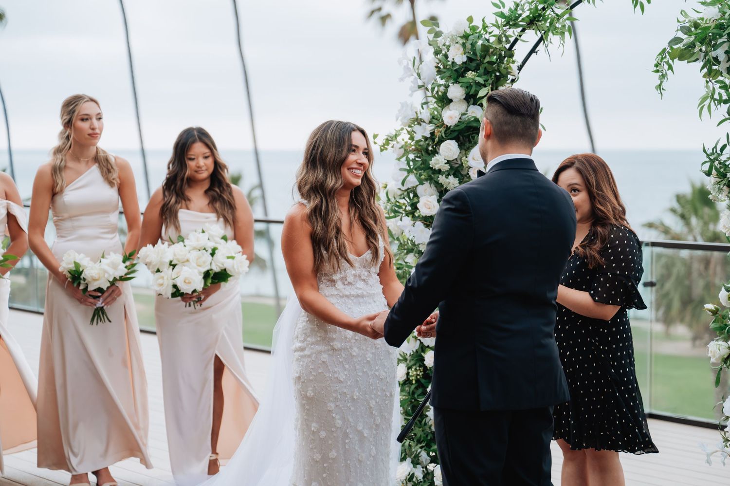 Wedding party members gather for formal photos at outdoor coastal venue.