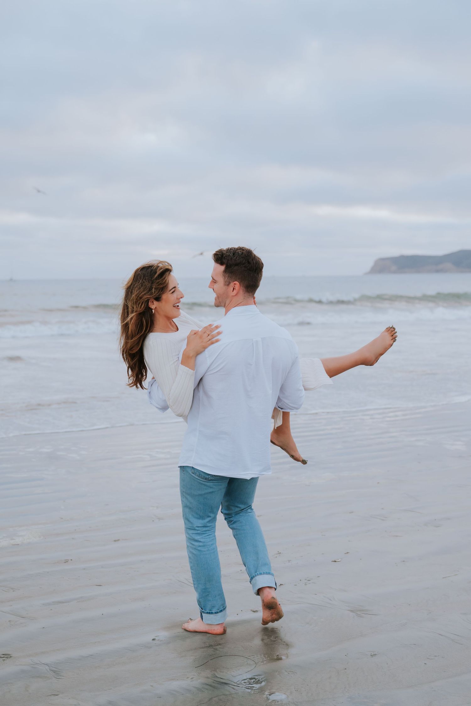 Playful couple splashes in ocean waves during beach photoshoot.