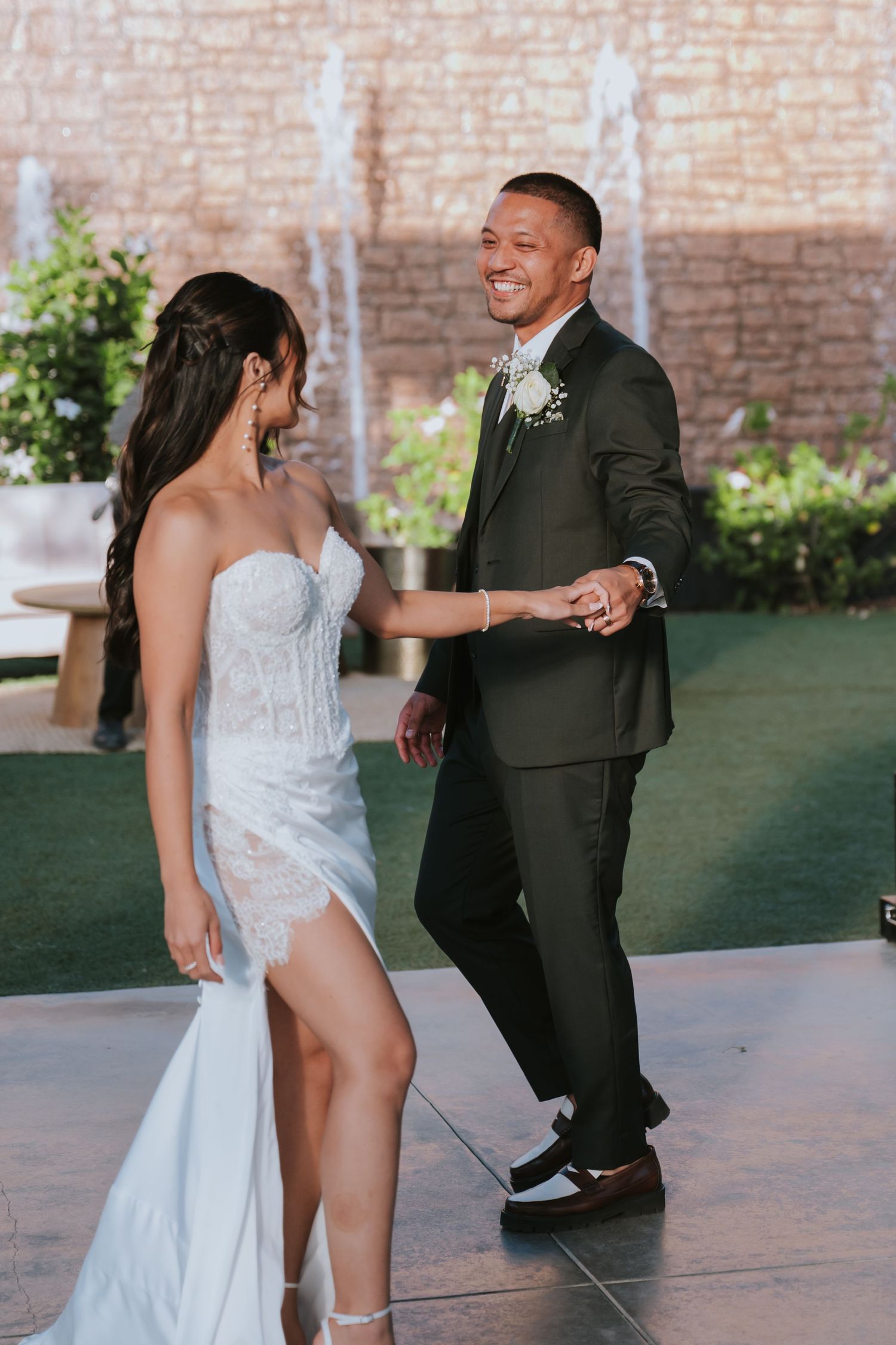 Wedding couple dancing together on an outdoor patio with brick wall backdrop.