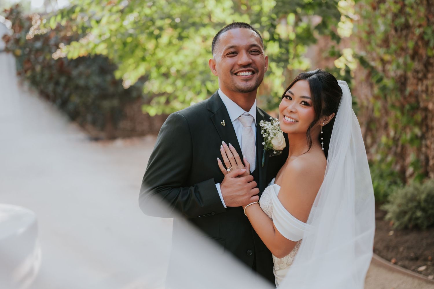 A joyful wedding couple shares a candid laughing moment together in an outdoor garden setting.