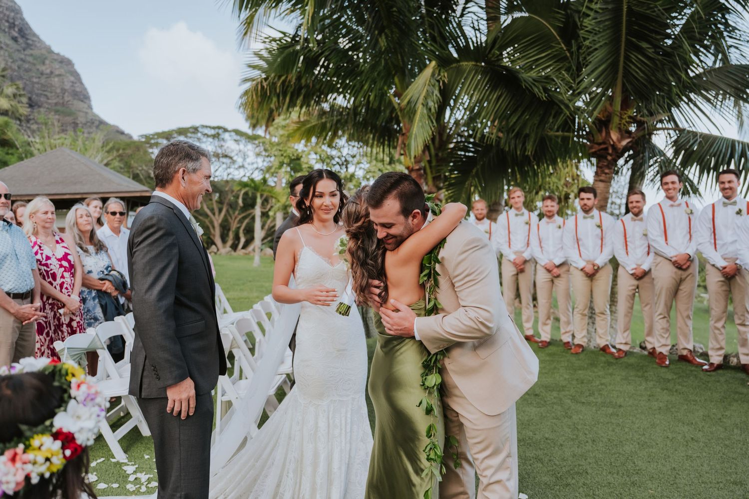 Tropical beach wedding ceremony in Hawaii with palm trees and mountains creating a stunning natural backdrop.