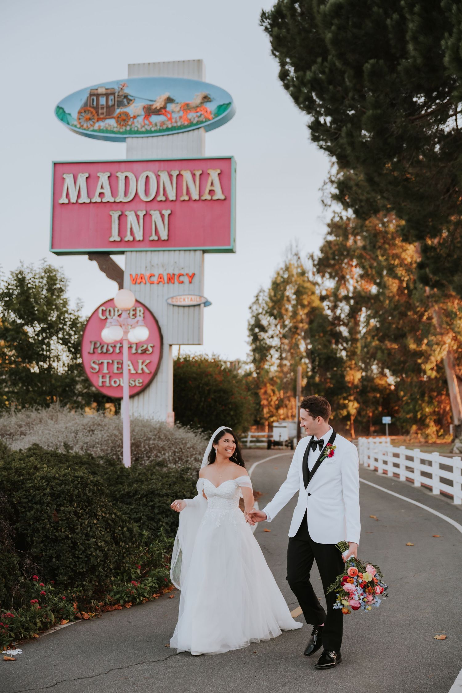 Newlywed couple poses playfully in front of vintage Madonna Inn motel sign during sunset photo session.