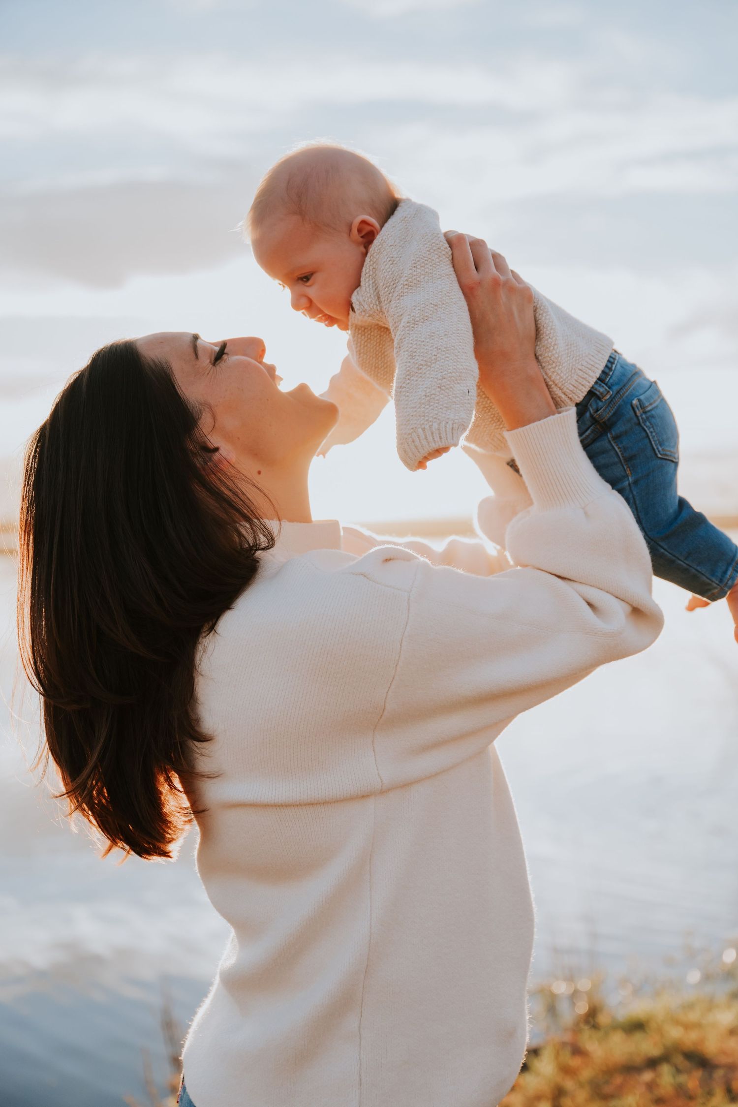 Parent and baby share joyful moment together against sunset sky.