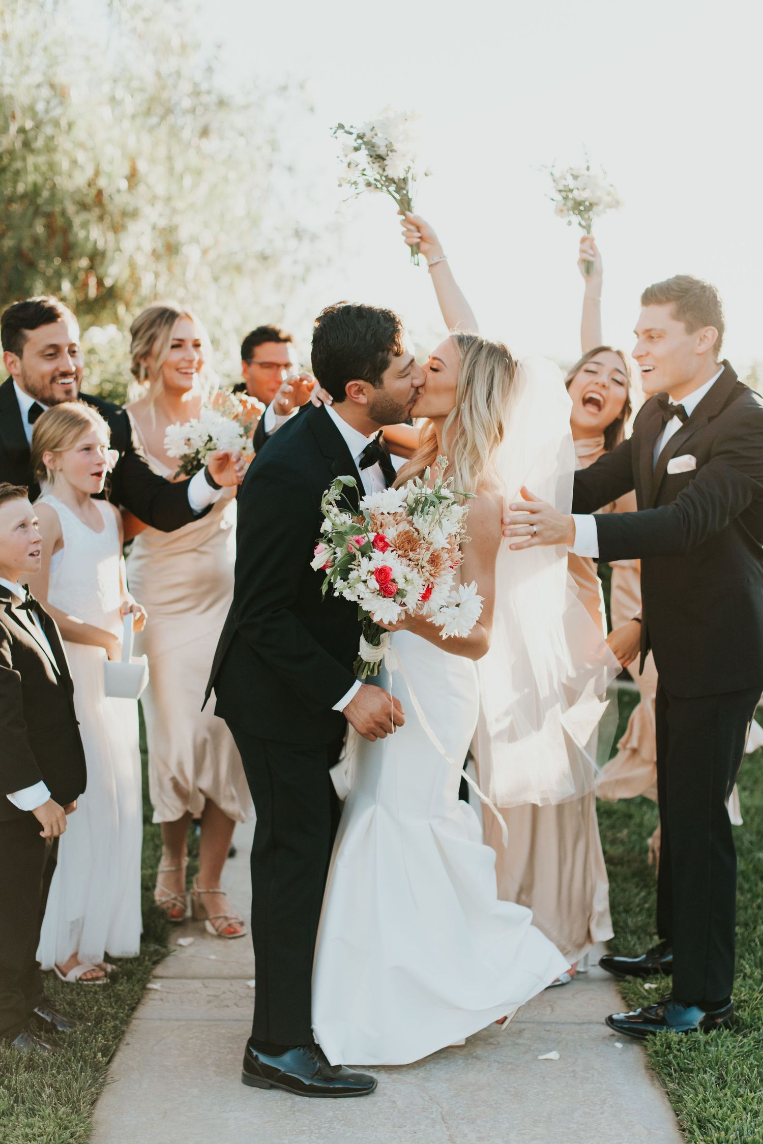 Wedding party celebrates joyfully with dancing and laughter during outdoor reception festivities.