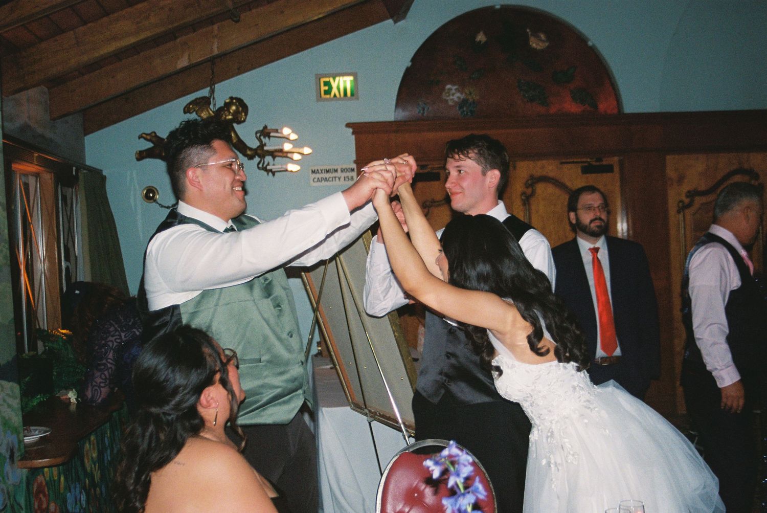 Wedding reception celebration in a rustic indoor venue with wooden beams and dim lighting.