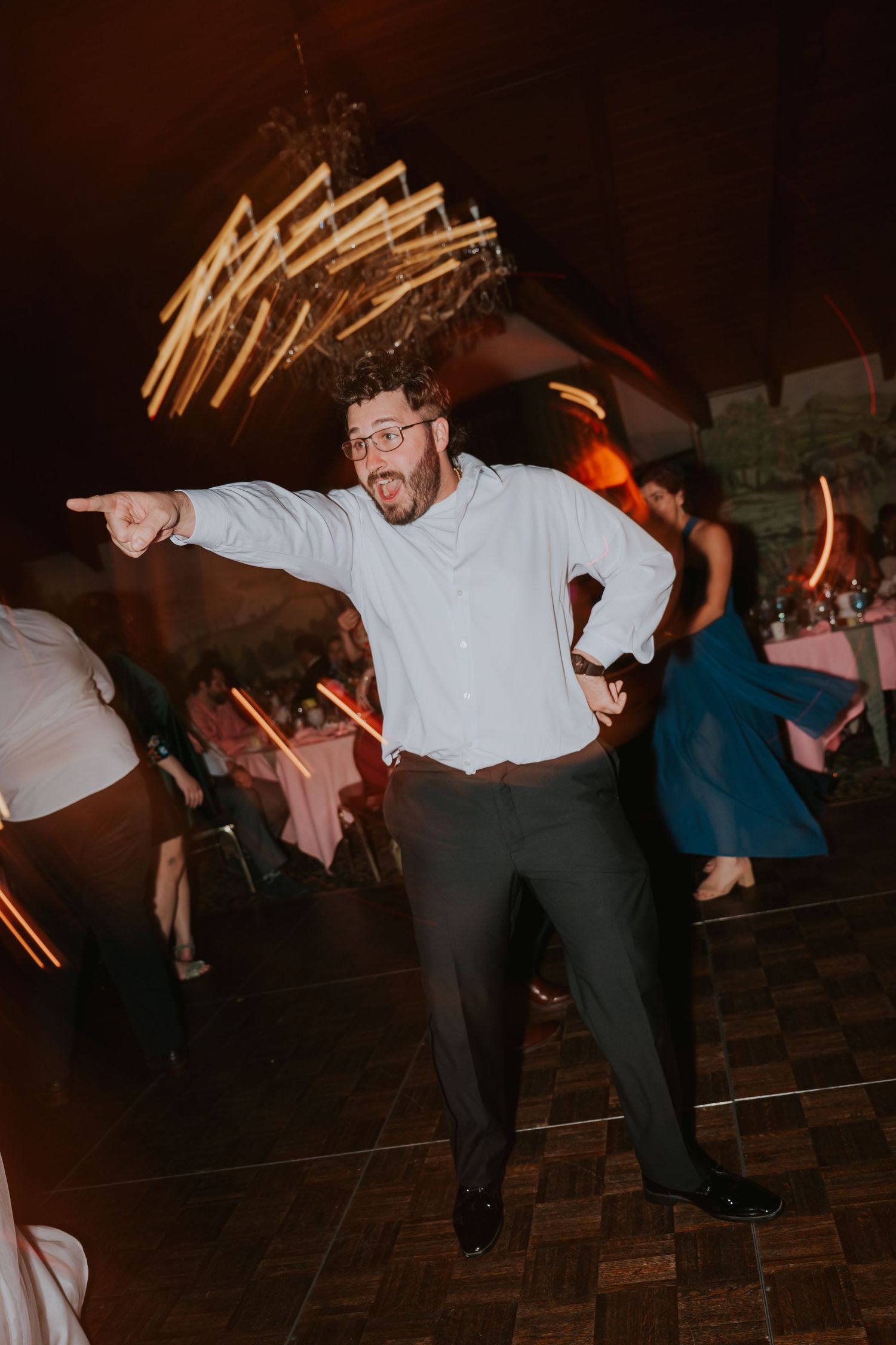 Wedding guests performing synchronized dance moves on a dark dance floor.