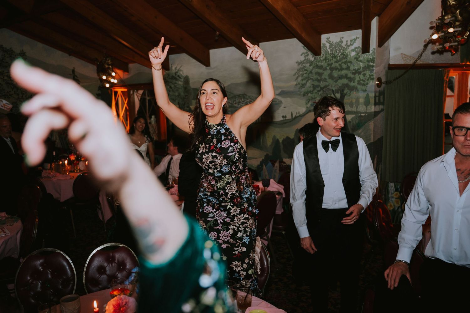 Wedding reception dance floor with guests celebrating under dim lighting and rustic wooden beams.