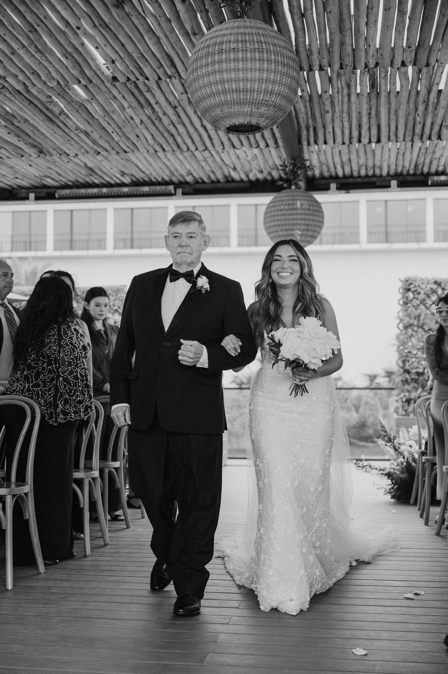 Black and white photo of wedding party walking down aisle in covered outdoor venue.