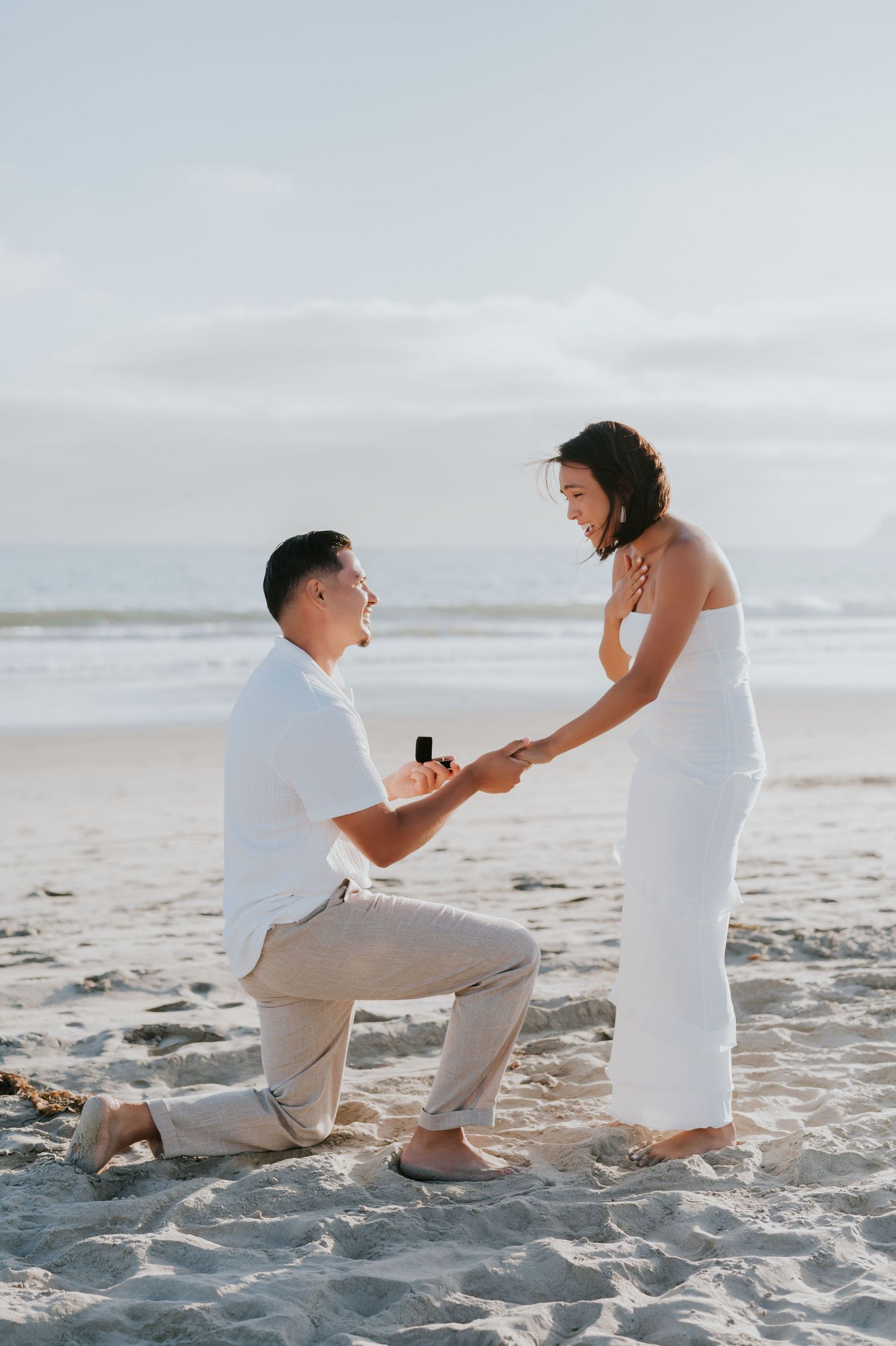 A romantic beach proposal sequence showing a couple on white sand with cloudy skies in the background.