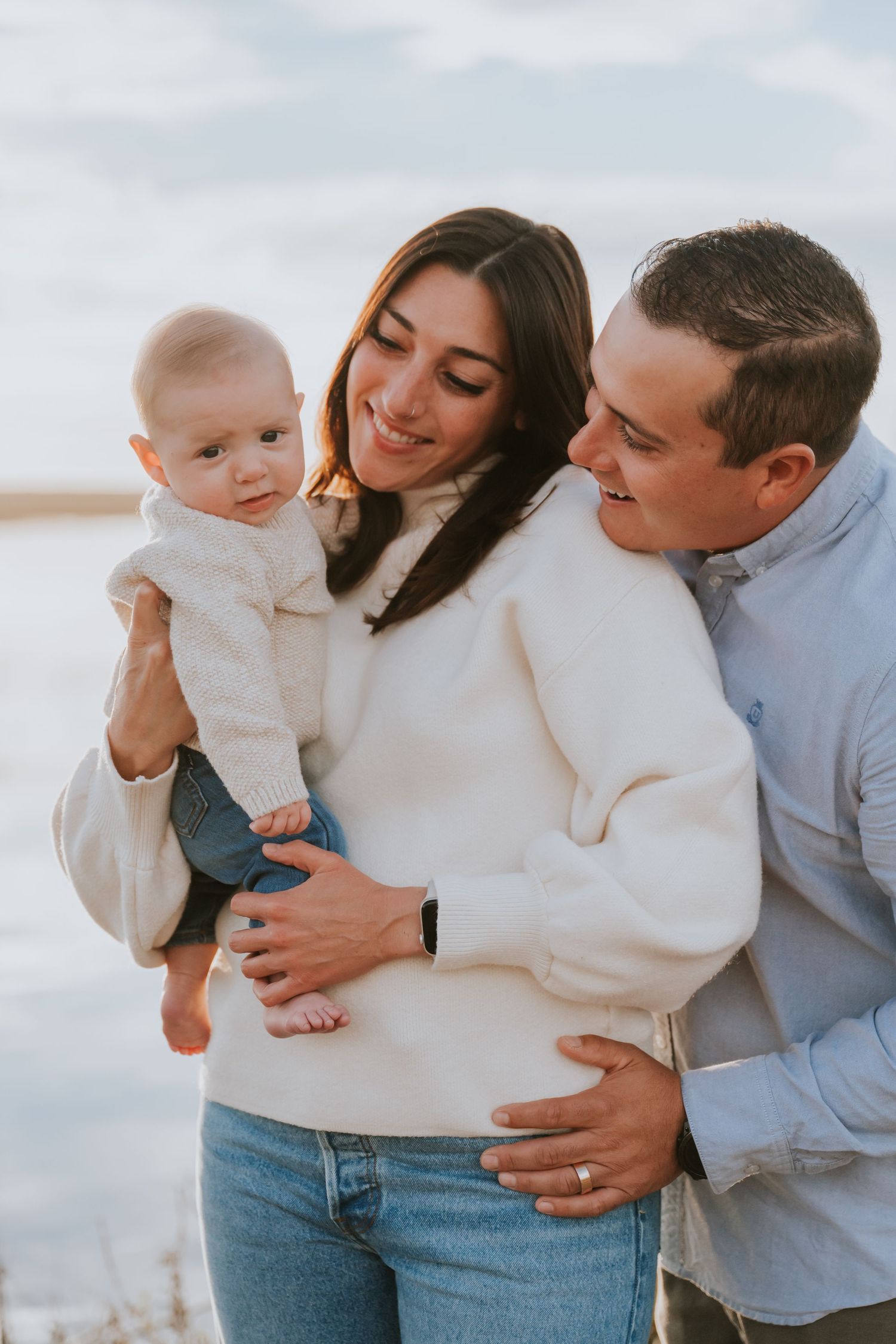 Family shares tender moment together at sunset by the ocean.
