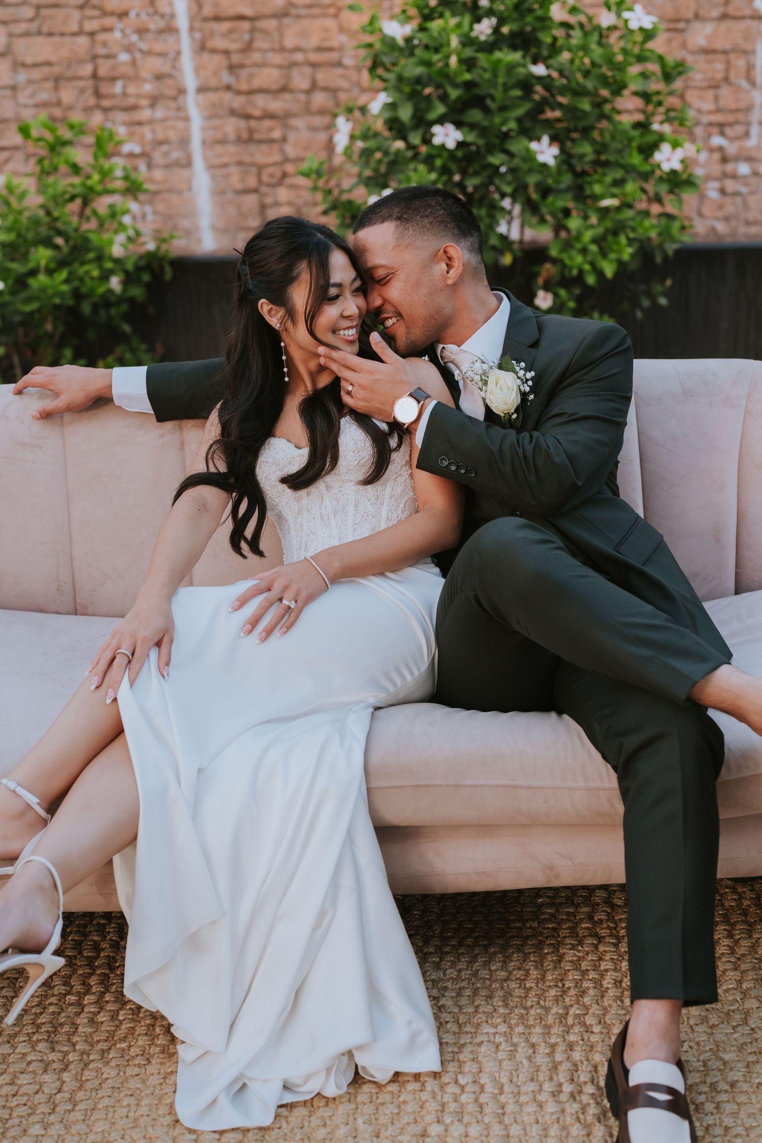 A romantic wedding photoshoot on a beige couch showing playful interaction between newlyweds.