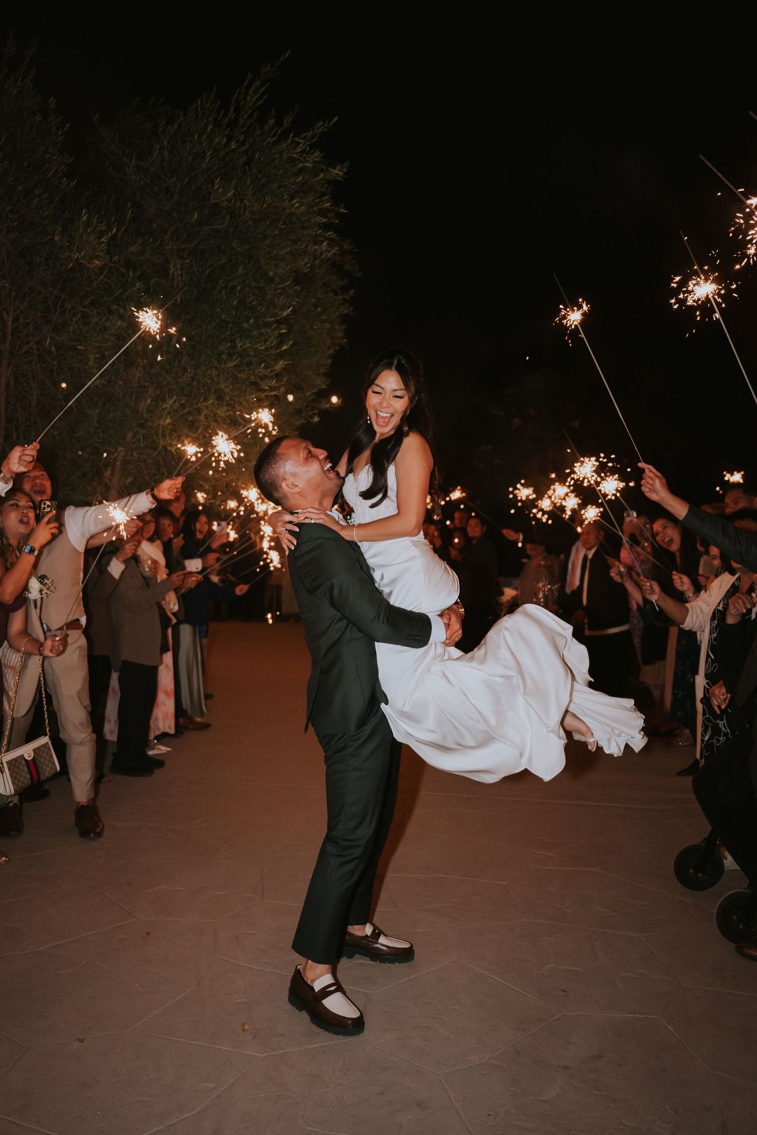Groom dips bride during sparkler exit at nighttime wedding celebration.