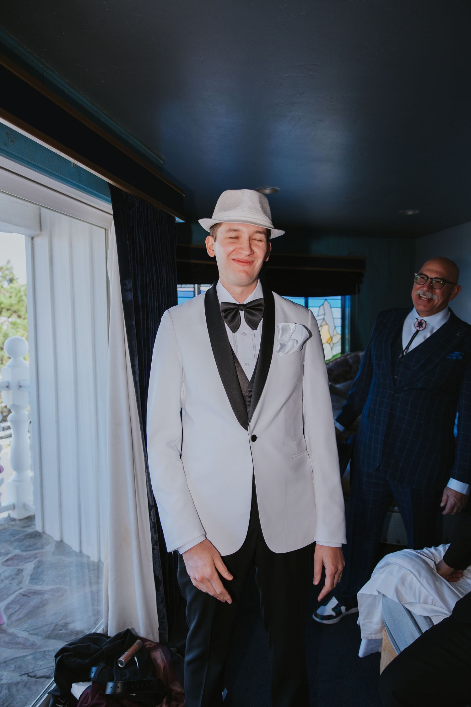 Wedding party members in formal white tuxedo jackets and black bow ties getting ready indoors.