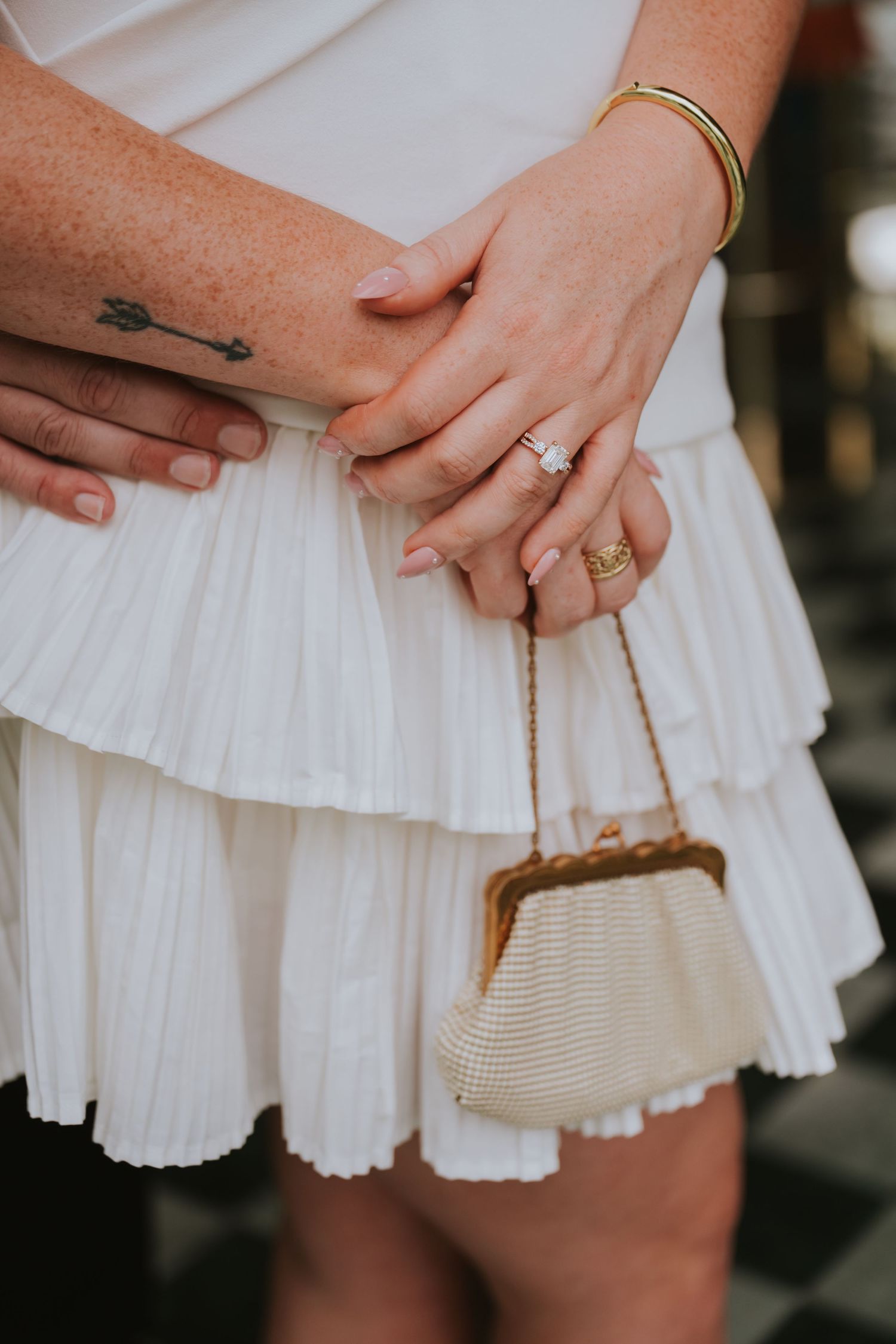 Close-up of bride's engagement ring, gold bangles, arrow tattoo, and vintage gold mesh clutch purse.