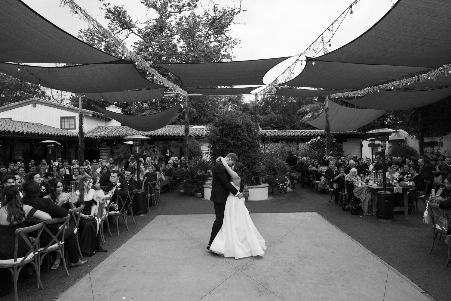 A couple shares their first dance at an outdoor wedding reception under fabric canopies.