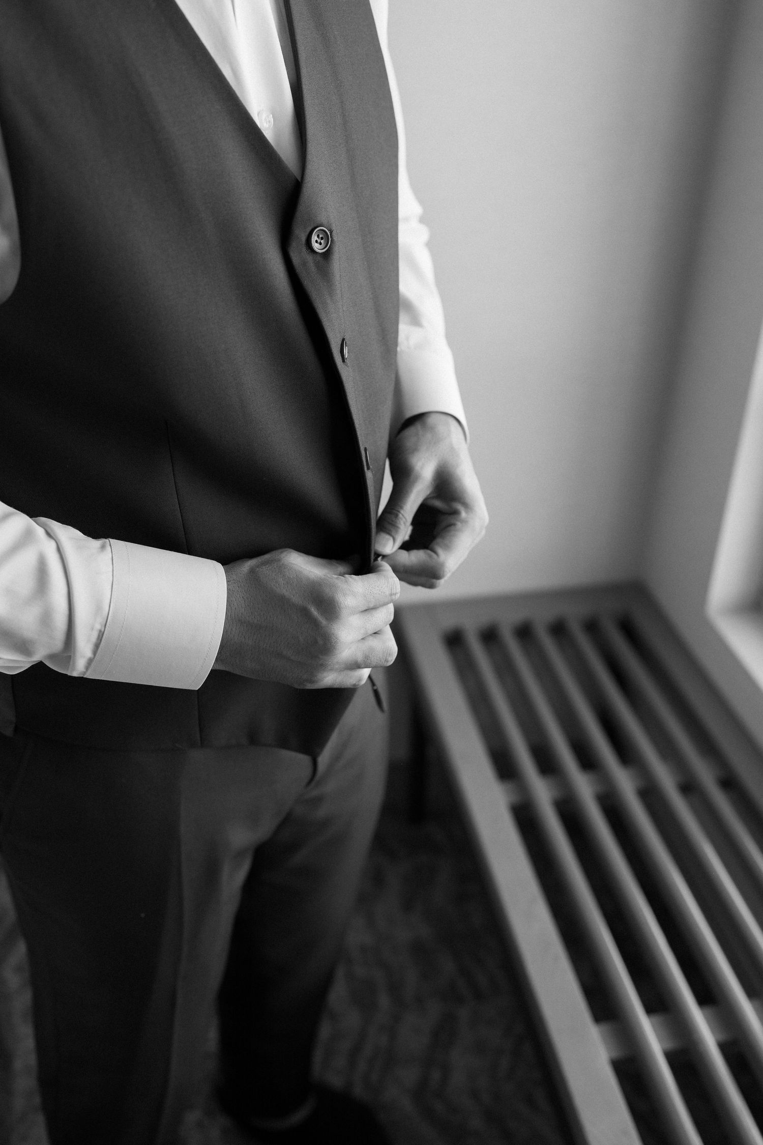 Black and white image showing someone adjusting a formal suit jacket and tie in a professional setting.