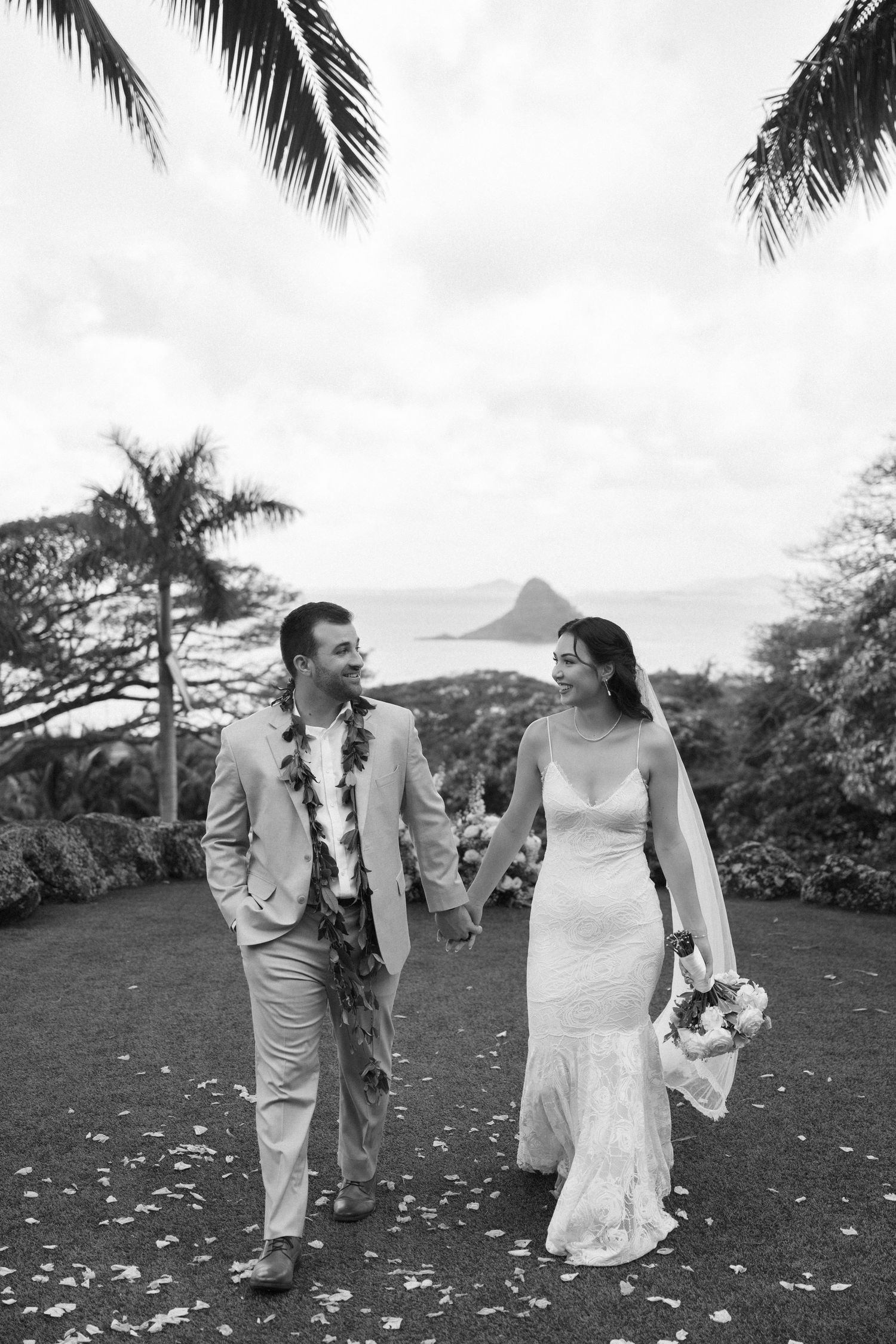 A black and white wedding photo series showing a couple dancing and laughing on a tropical garden lawn.