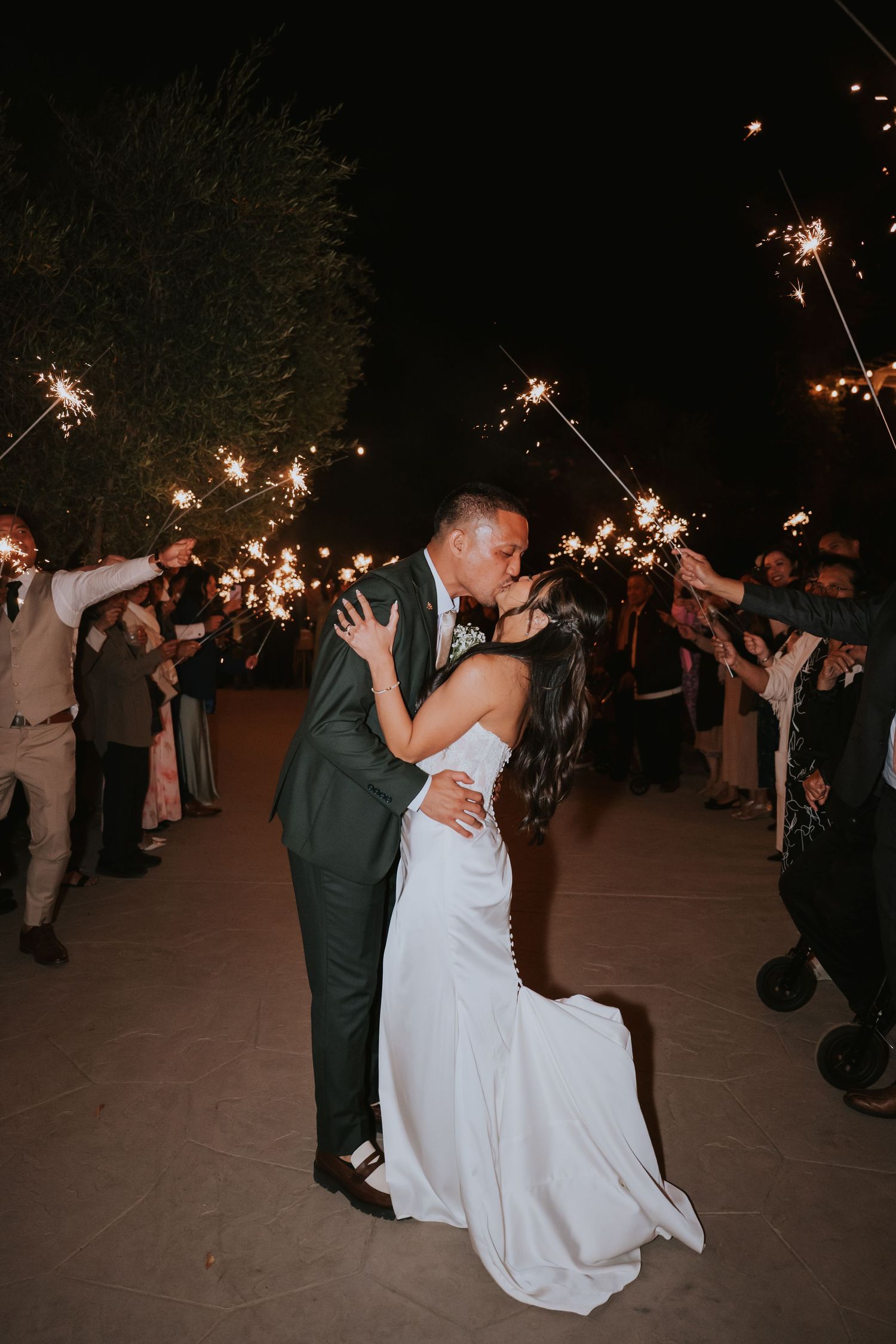 Couple dances together at nighttime wedding celebration surrounded by guests holding sparklers.