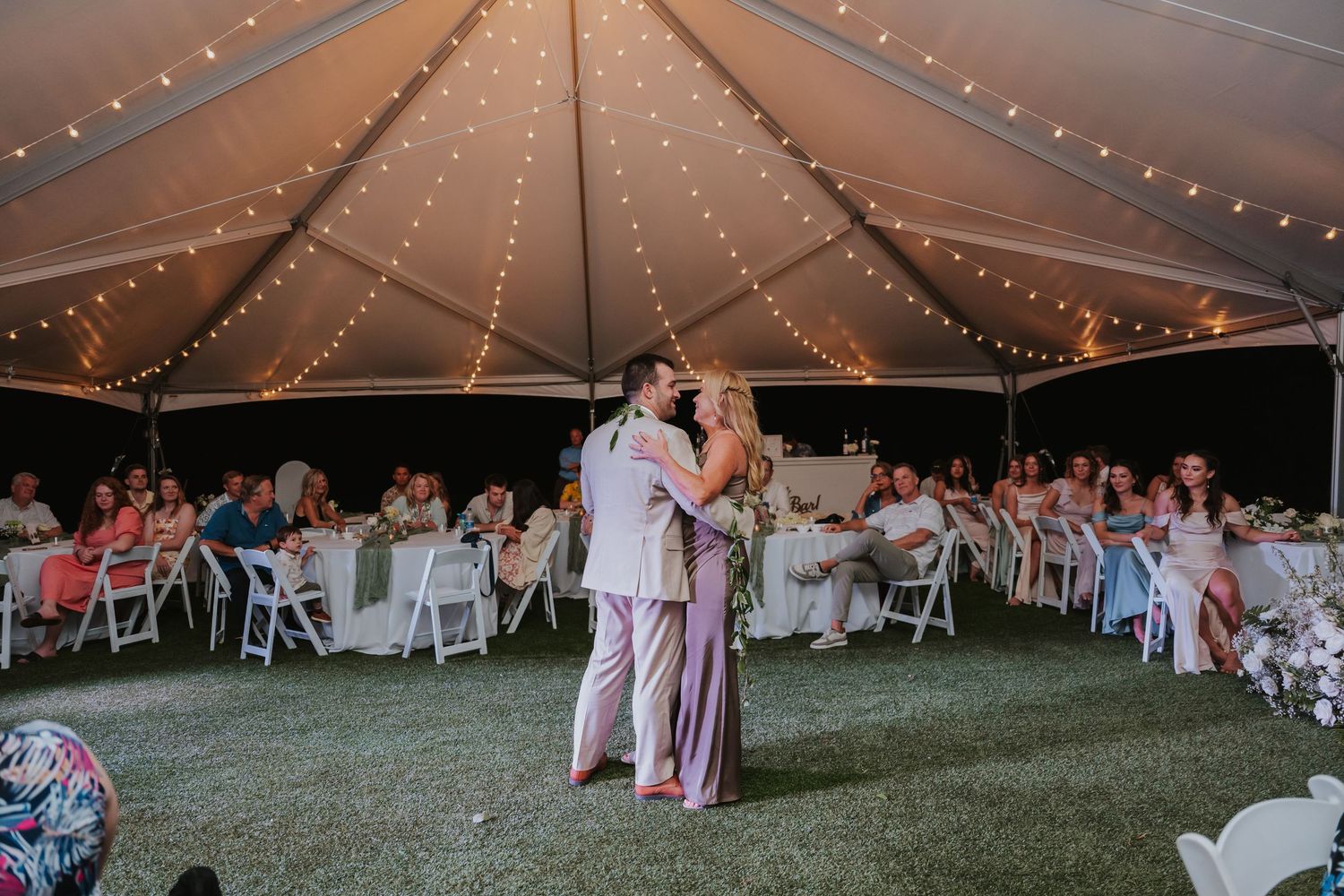 Evening wedding reception under a large tent with string lights and guests dancing on the lawn.