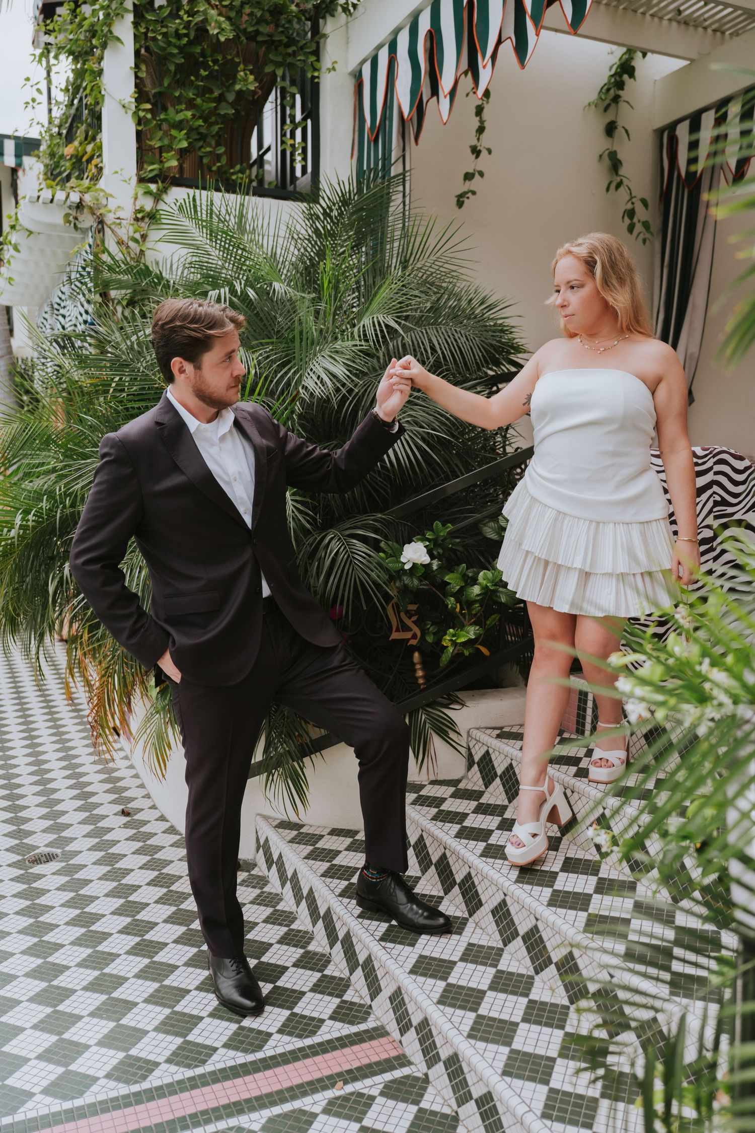 Bride and groom dancing in a tropical courtyard with checkered tile floors and lush greenery.