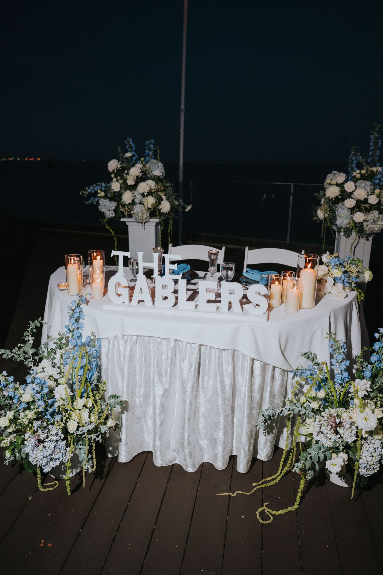 Elegant wedding sweetheart table with white floral arrangements, candles, and THE GABLERS sign at a nighttime reception.