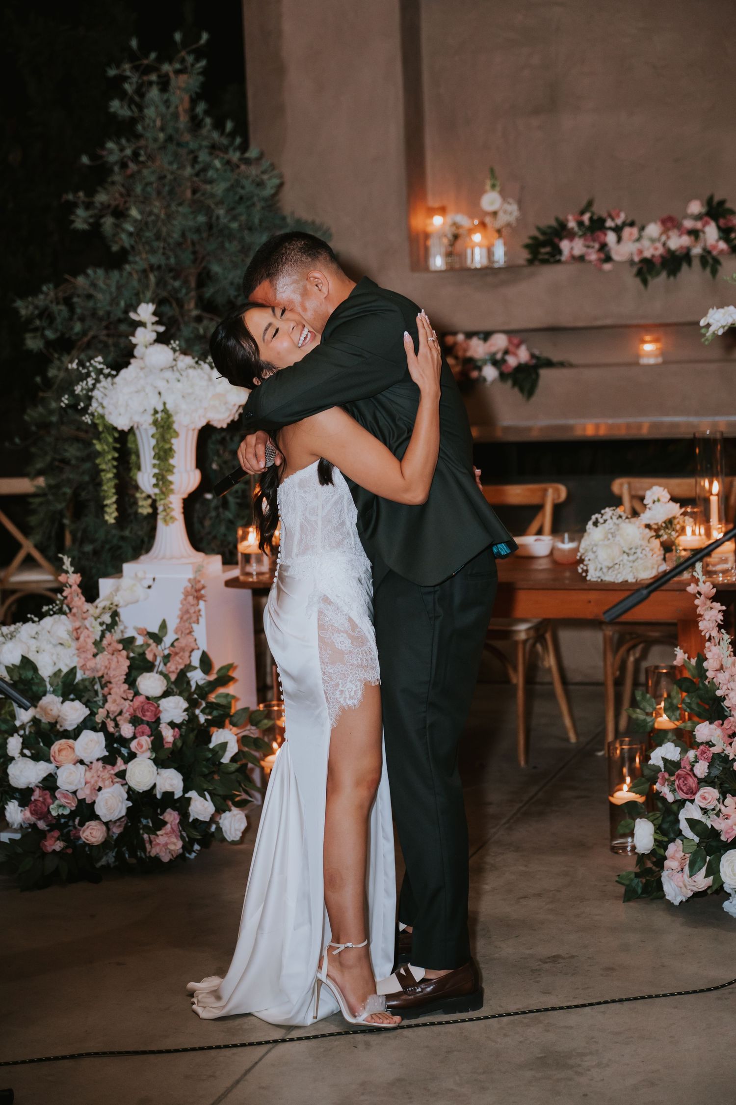 A romantic wedding couple embraces on the dance floor surrounded by elegant floral arrangements and candlelight.