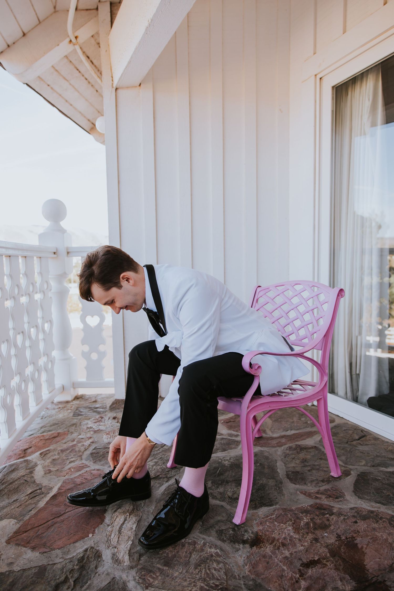 A sequence showing someone in formal attire adjusting their shoe while sitting on a porch with a pink chair.
