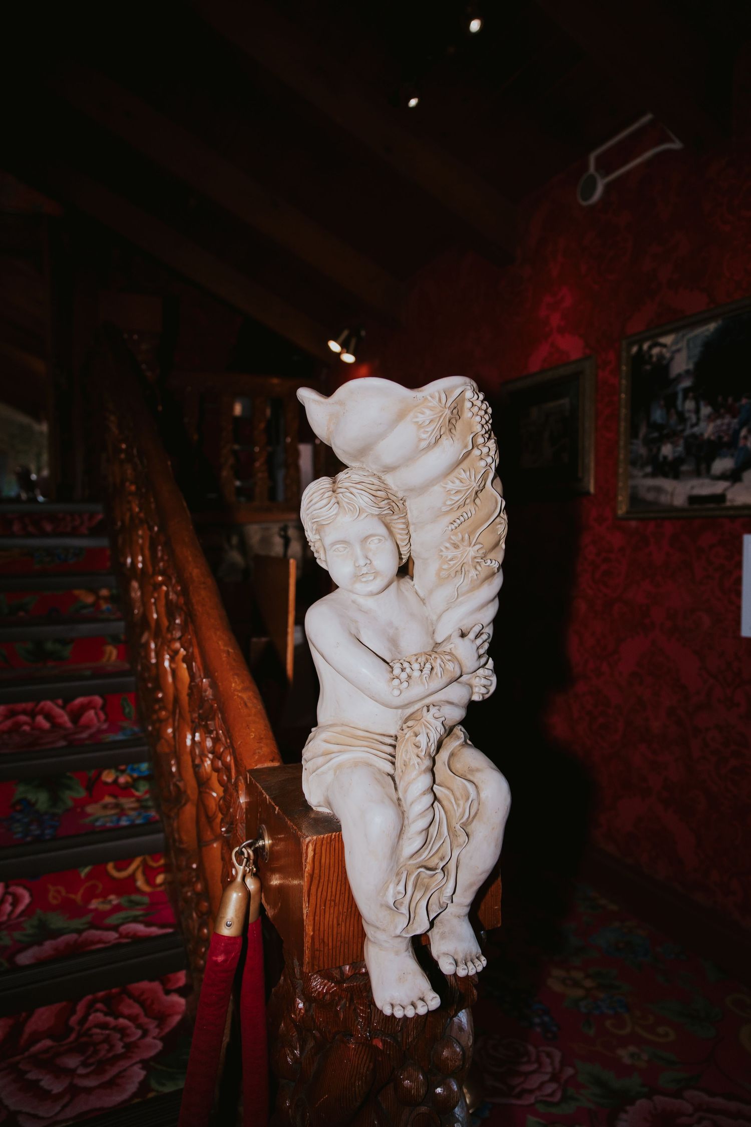 White cherub statues in a dimly lit room with red walls and dramatic lighting create an eerie atmosphere.