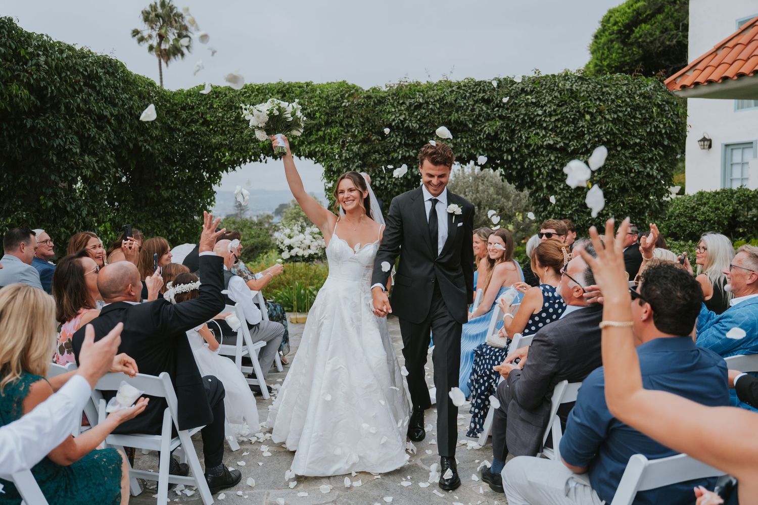 Guests celebrate and release white balloons during an outdoor wedding ceremony at a scenic garden venue.
