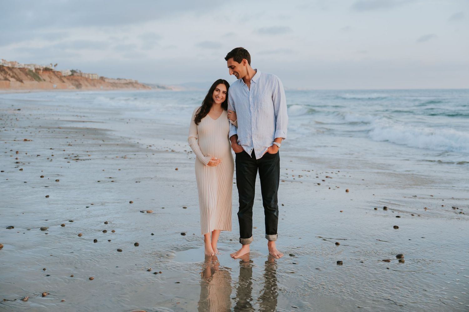 Couple walking hand in hand along peaceful beach shoreline at sunset.