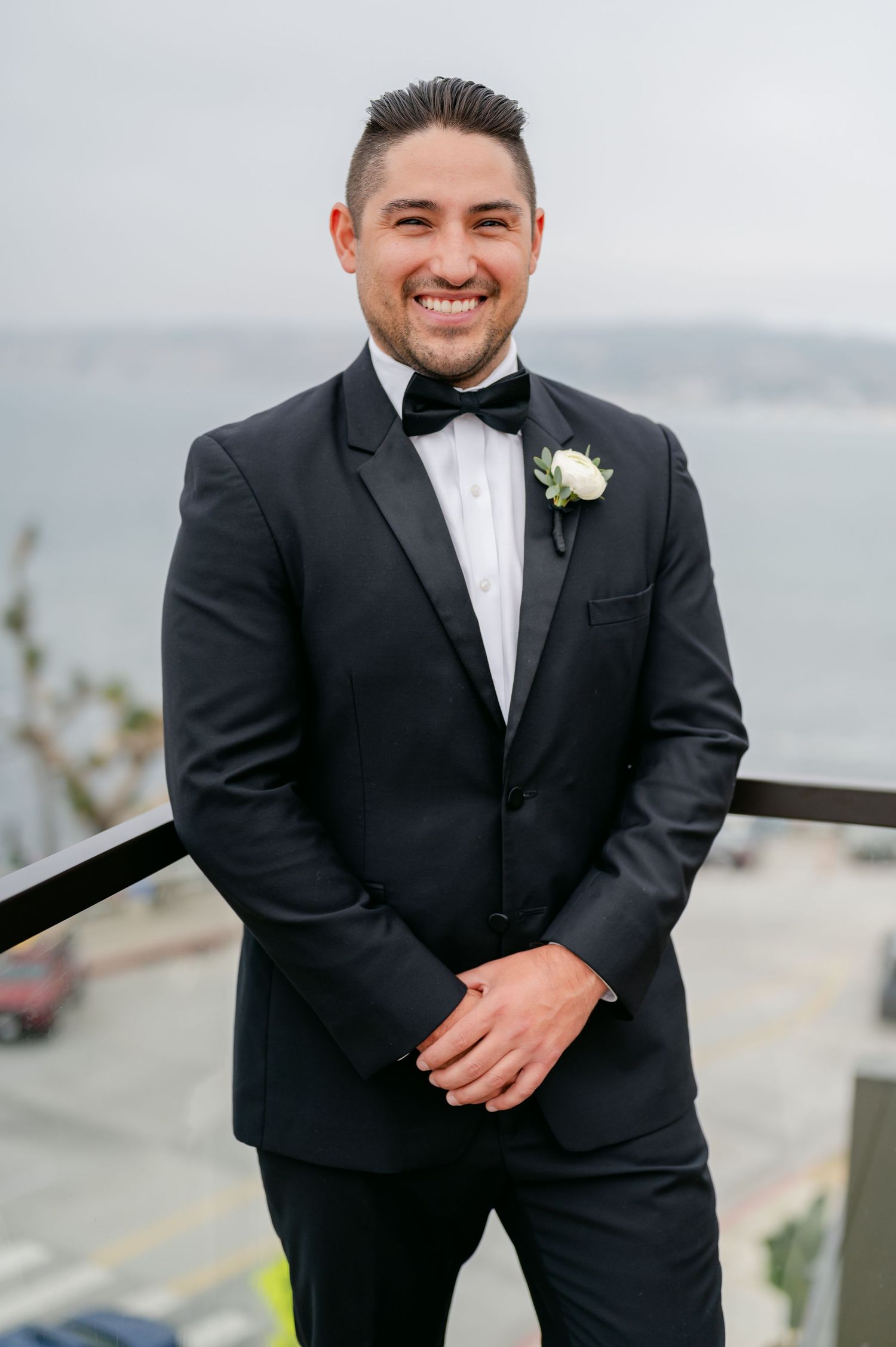 Groom in classic black tuxedo and white boutonniere smiles during outdoor wedding portraits.